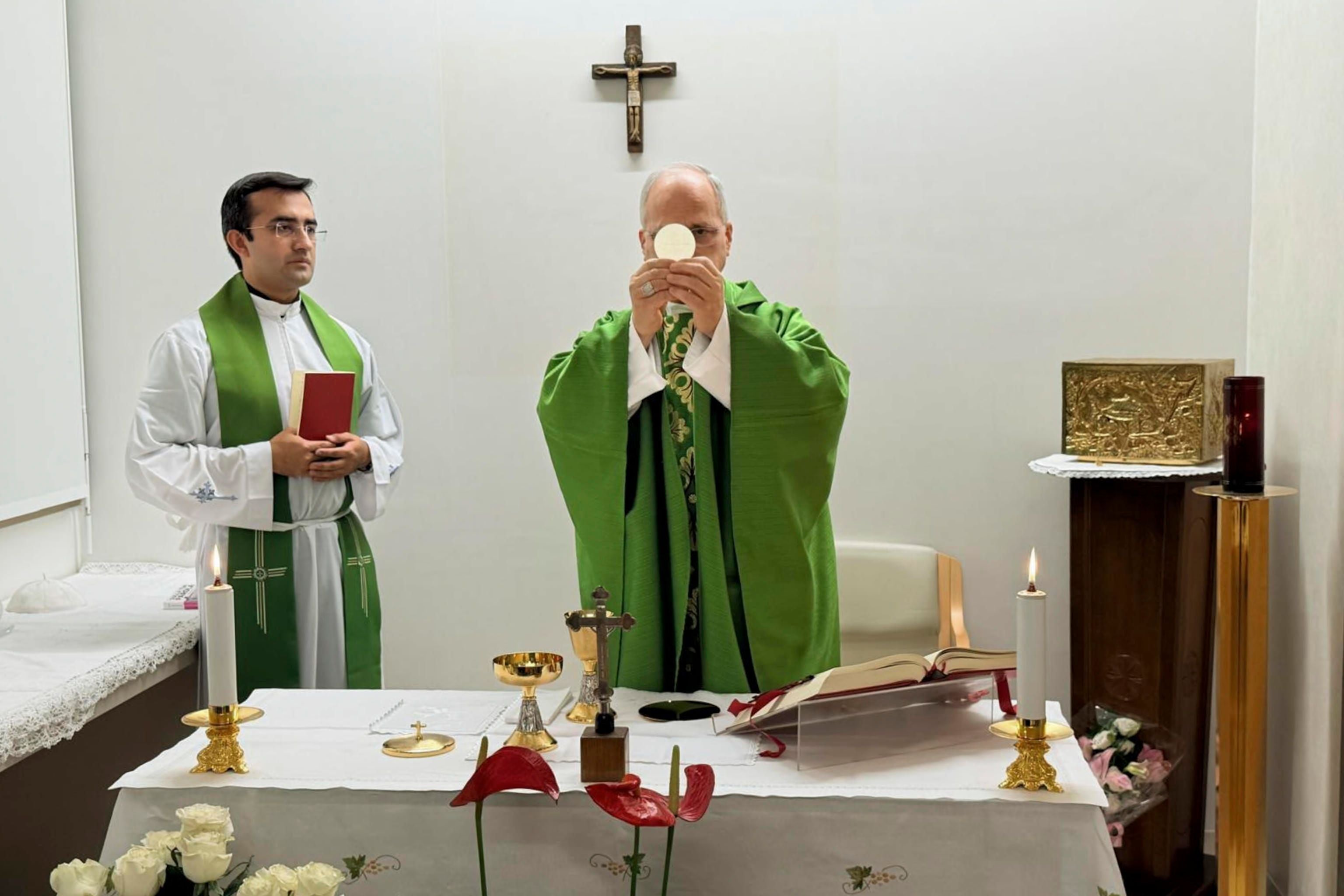 Zwei Priester feiern eine Messe an einem Altar mit Kreuz, Kerzen und Kelch in einer Kapelle.