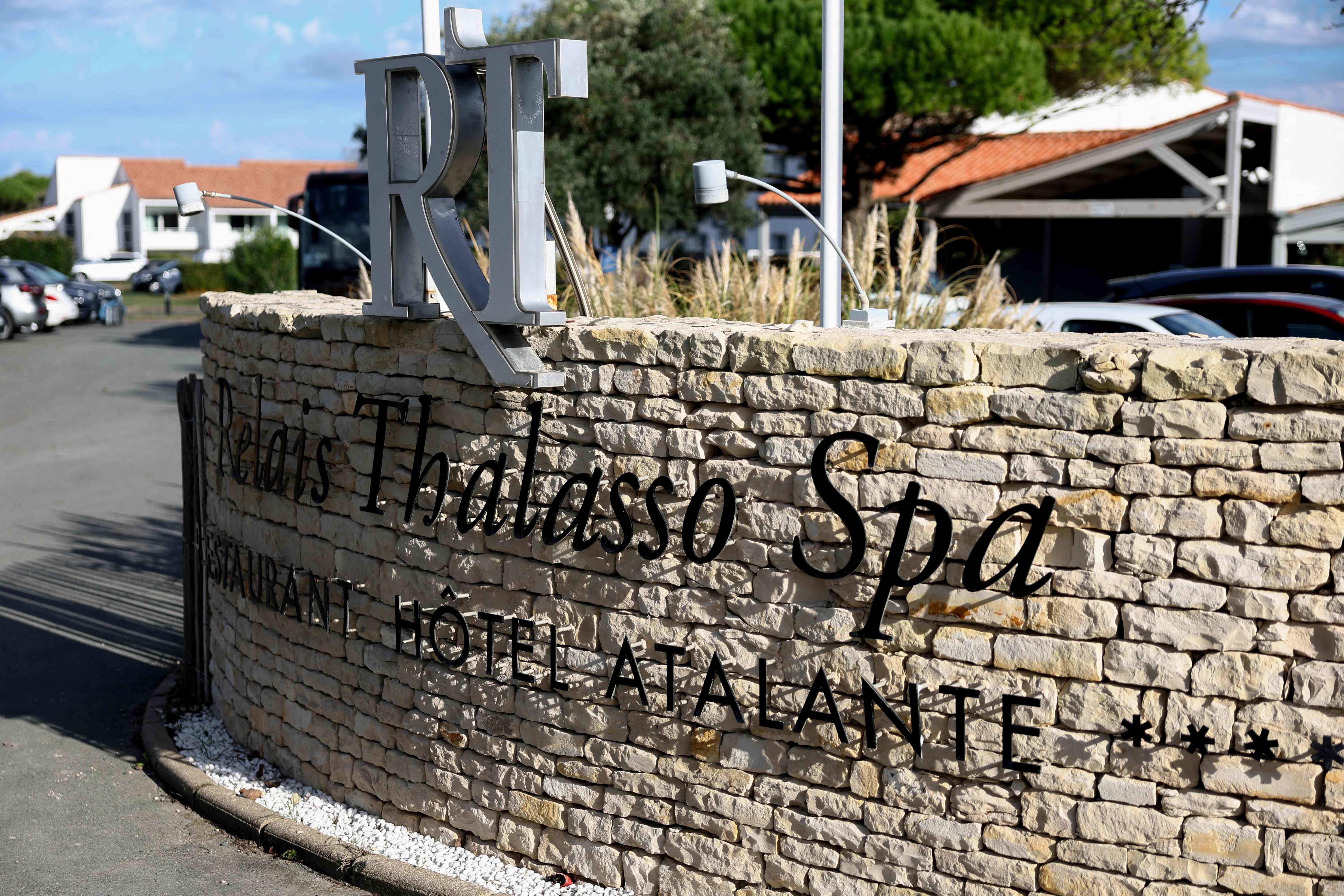 Steinmauer mit der Aufschrift "Relais Thalasso Spa RÉTA HOTEL ATALANTE" vor Hotelgebäuden.
