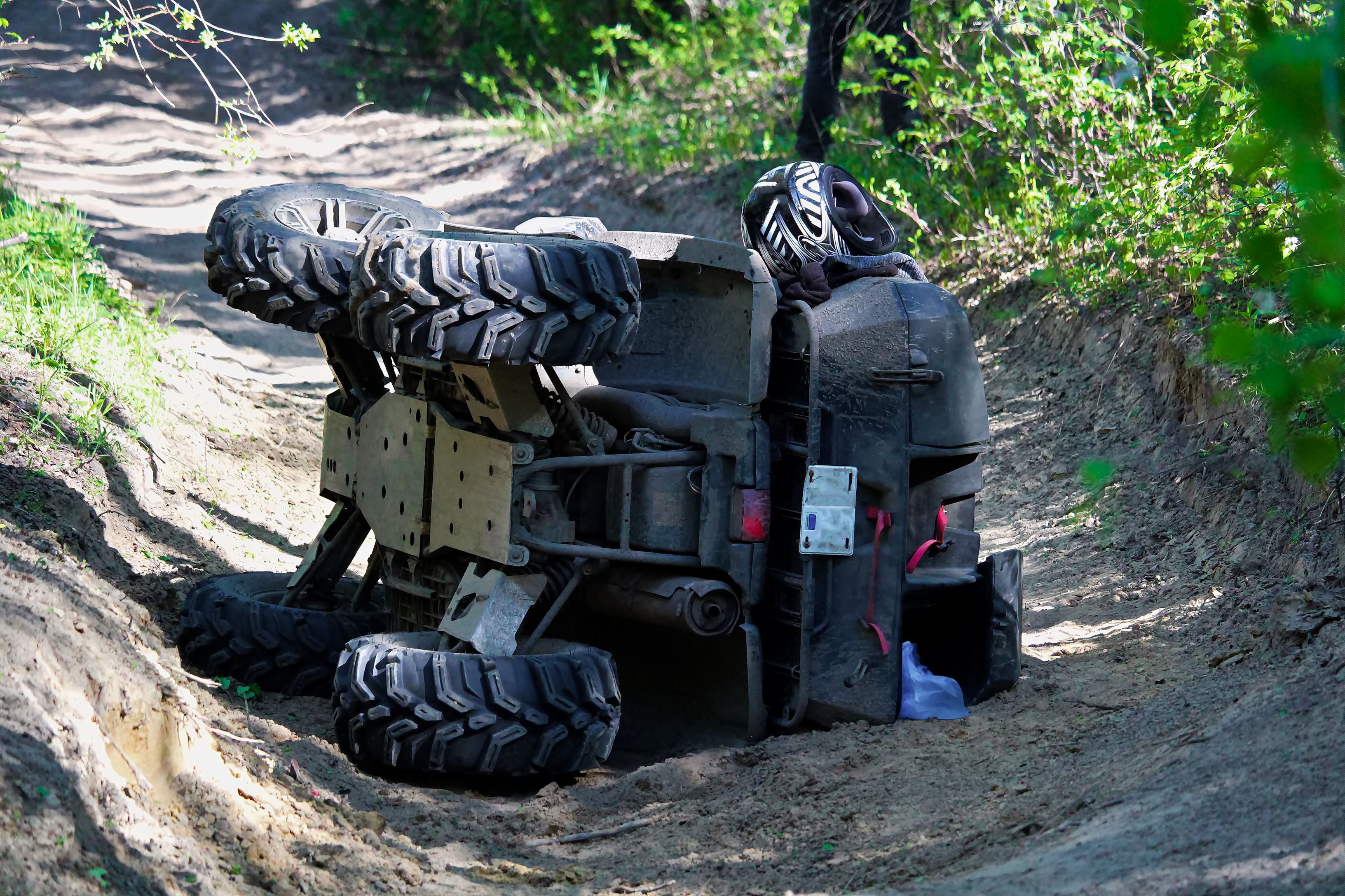 Ein Quad liegt nach einem Unfall seitlich auf einem sandigen Weg im Wald.