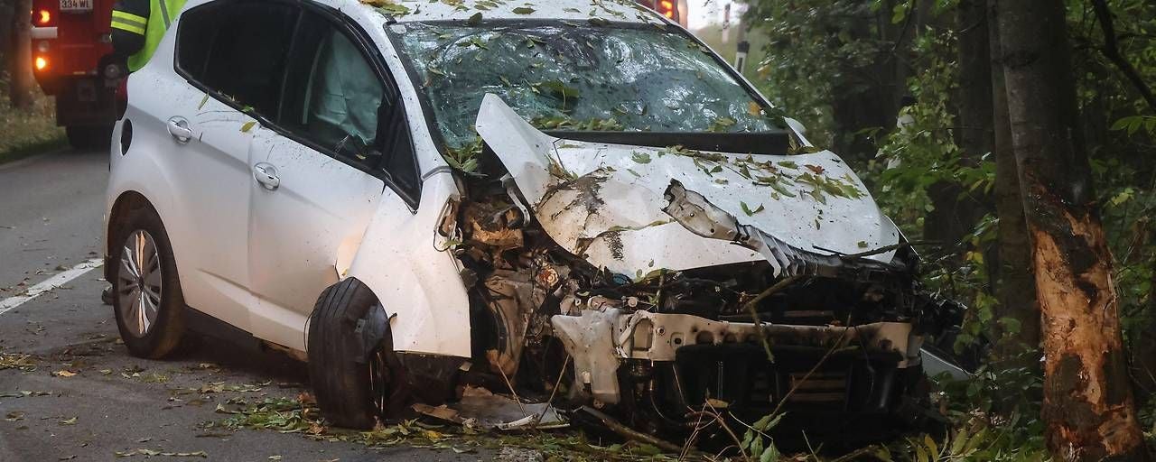 Ein weißes Auto ist frontal stark beschädigt, nachdem es gegen einen Baum geprallt ist.
