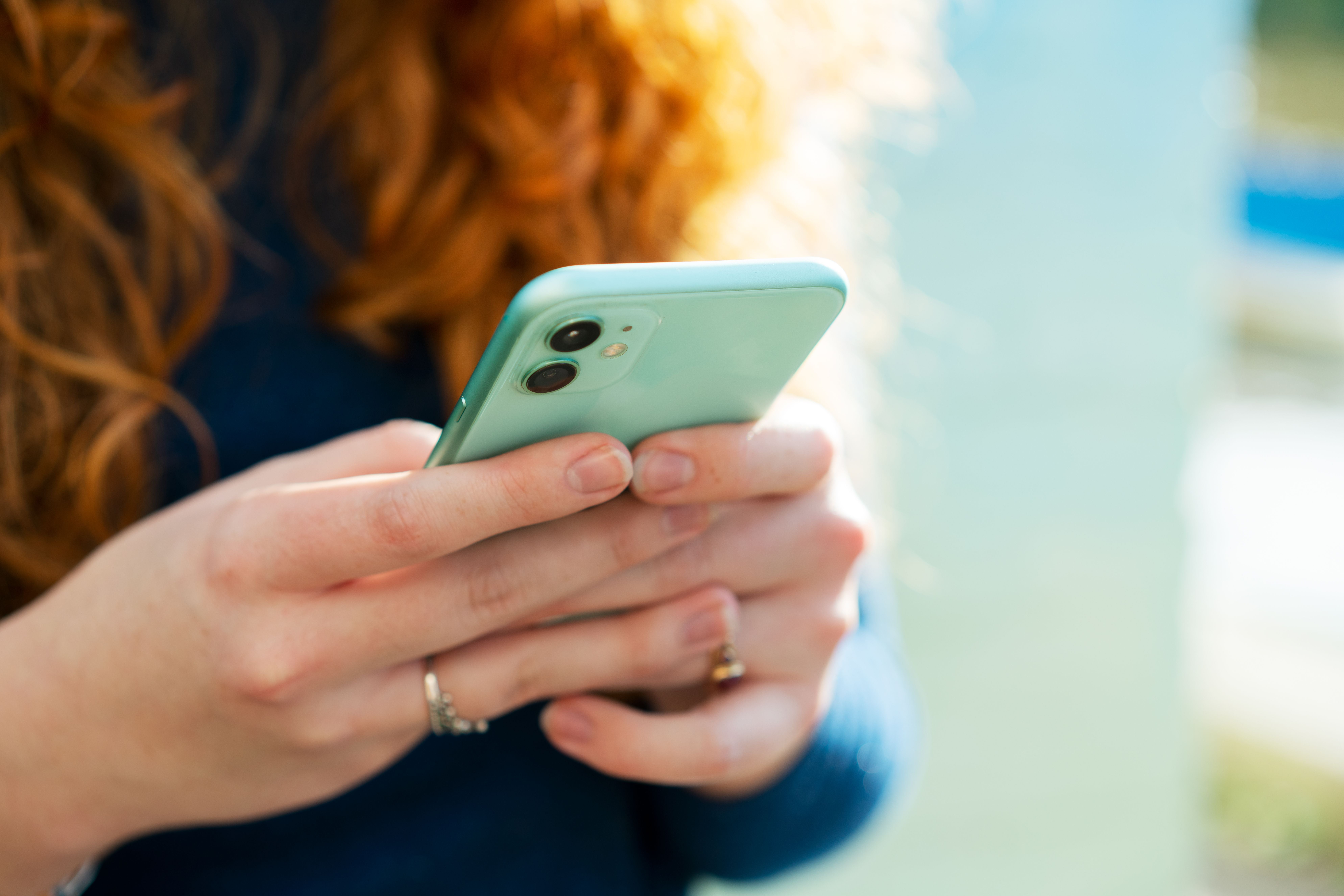 Frau mit roten Haaren hält ein grünes Smartphone in beiden Händen.
