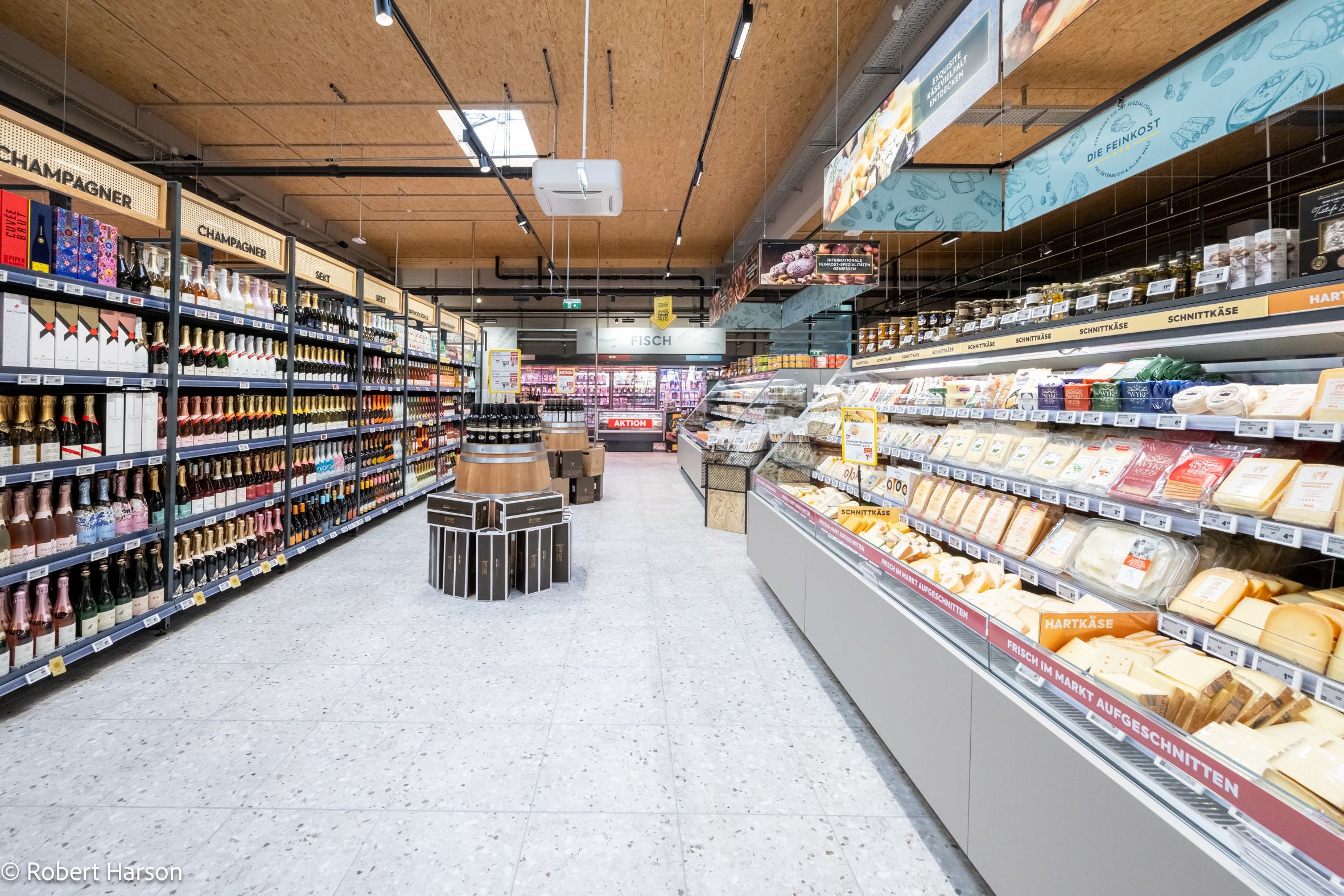 Blick in einen Supermarkt mit Weinregalen links und einer Käsetheke rechts.
