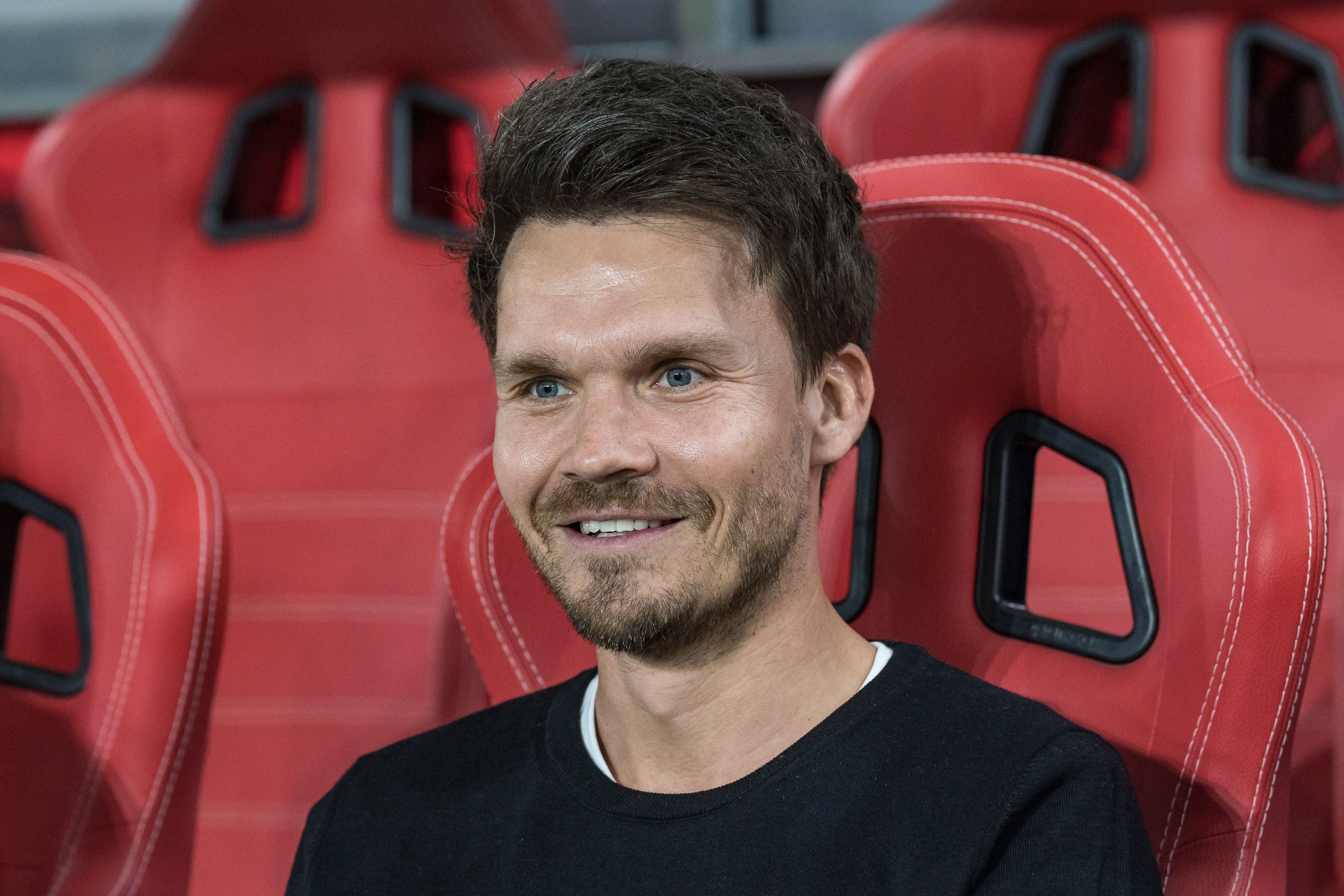 Ein lächelnder Mann sitzt auf einem roten Stadionstuhl.