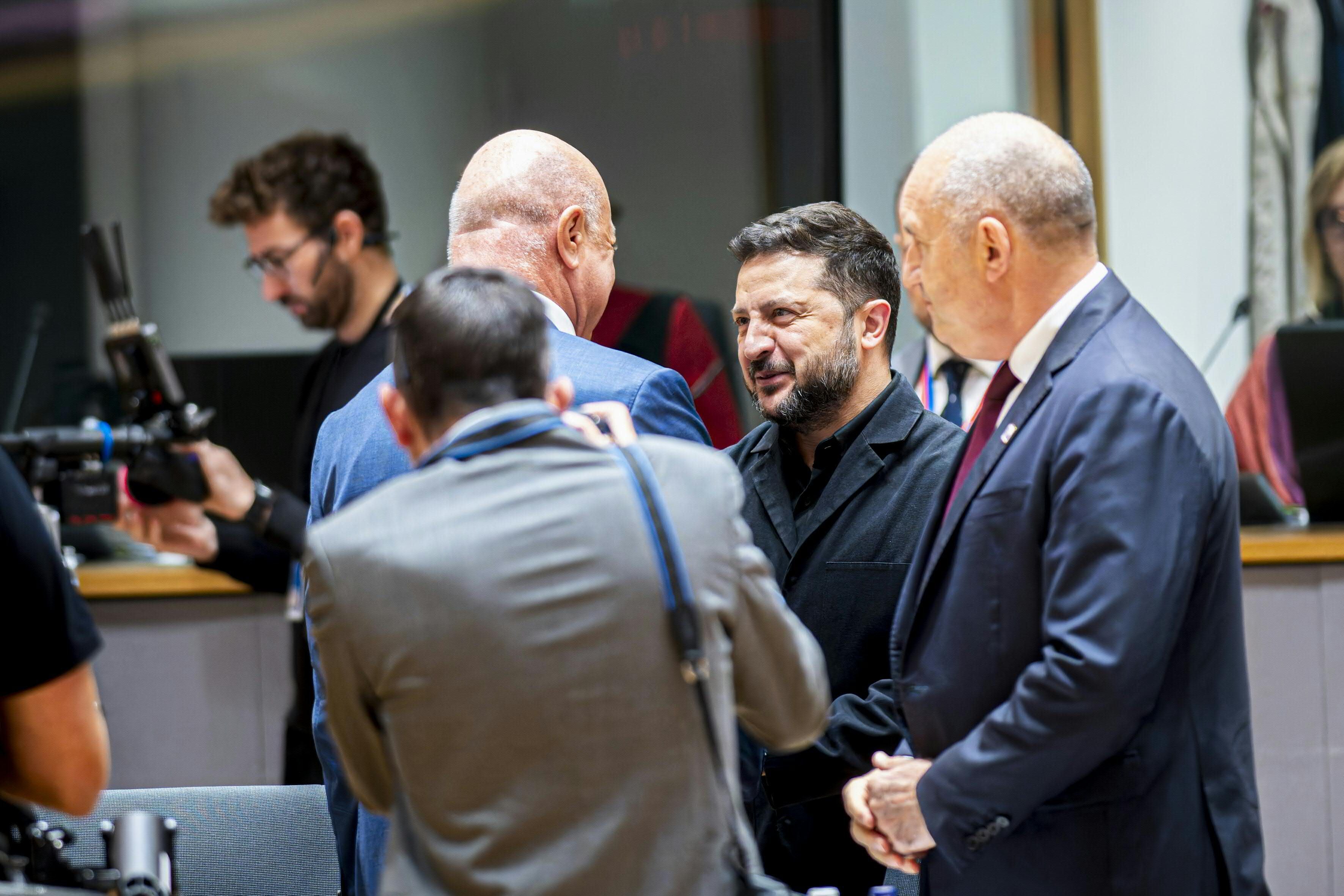 Mehrere Männer im Anzug unterhalten sich bei einem EU-Gipfel in einem Konferenzraum.