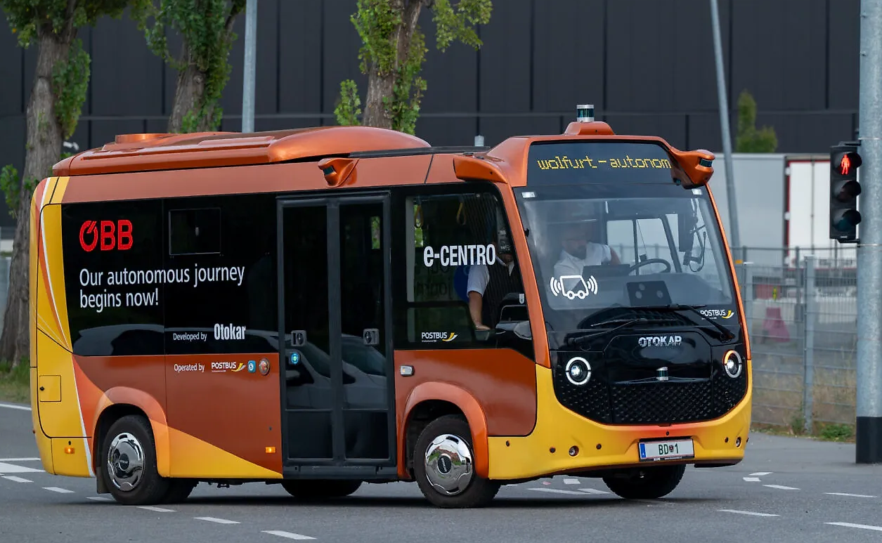 Kleiner autonomer Linienbus von ÖBB fährt auf einer Straße in Wolfurt bei grünem Licht.