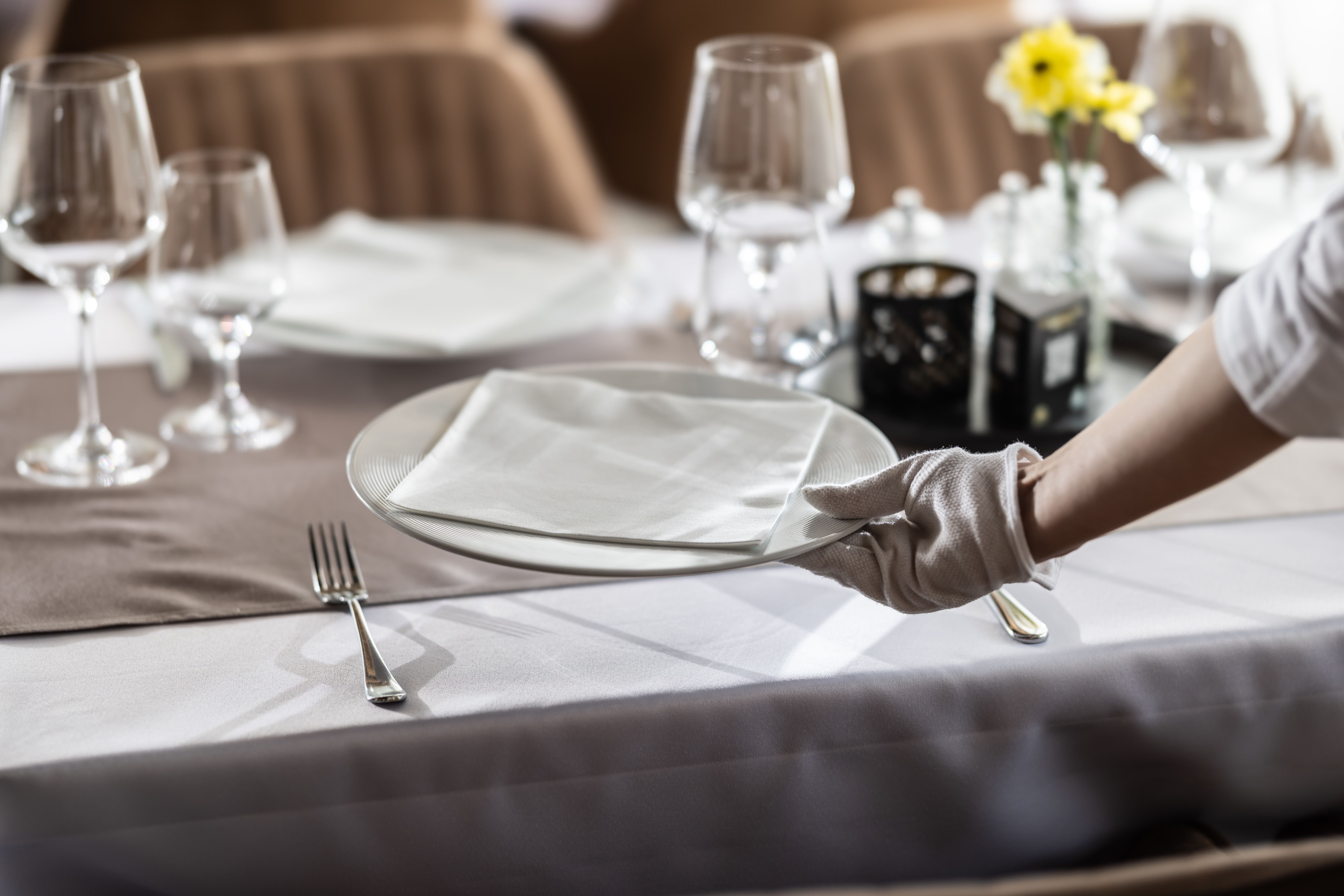 Ein Kellner deckt einen festlich gedeckten Tisch mit Teller und Stoffserviette im Restaurant.