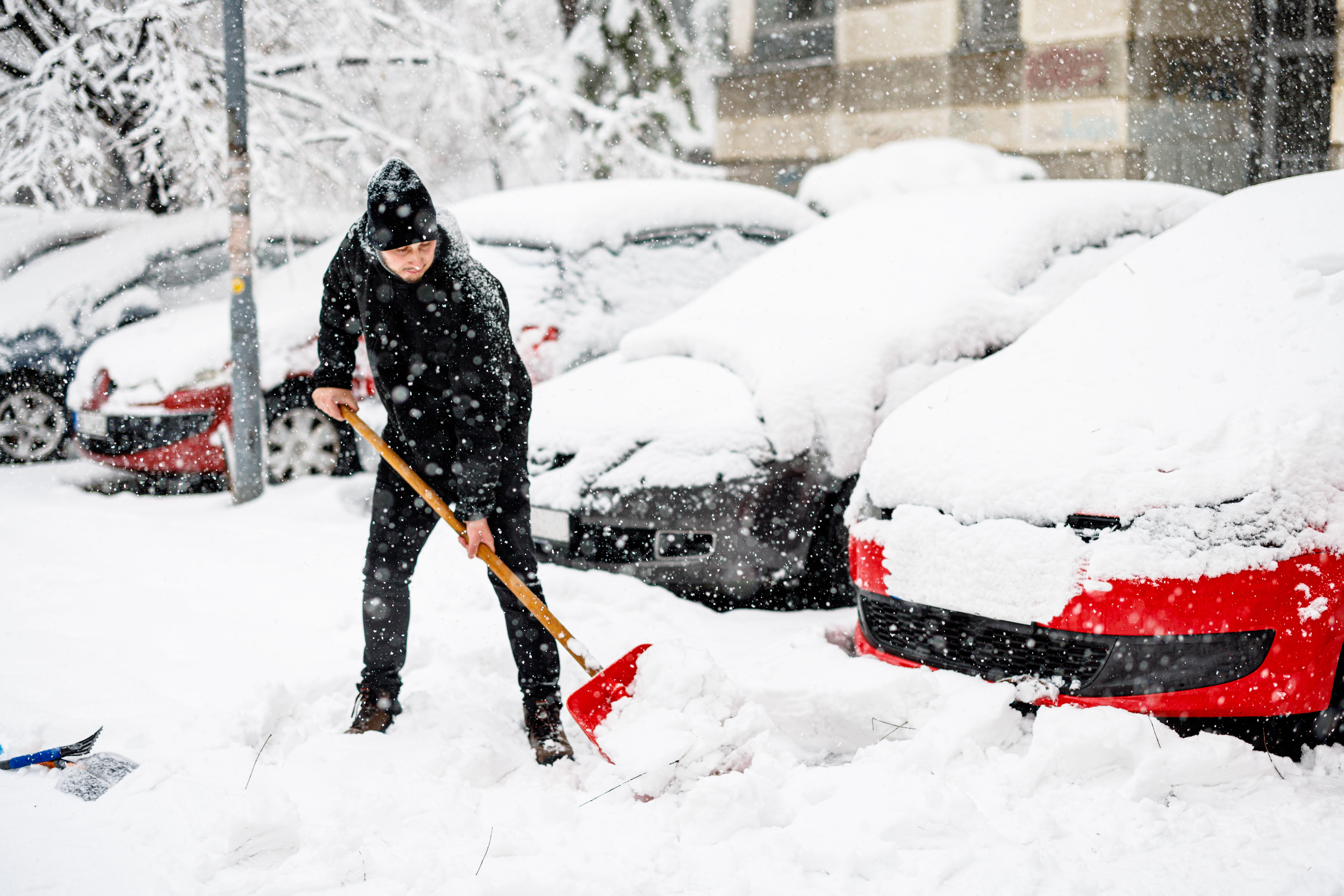 Ein Mann schippt Schnee vor verschneiten Autos an einem kalten Wintertag.