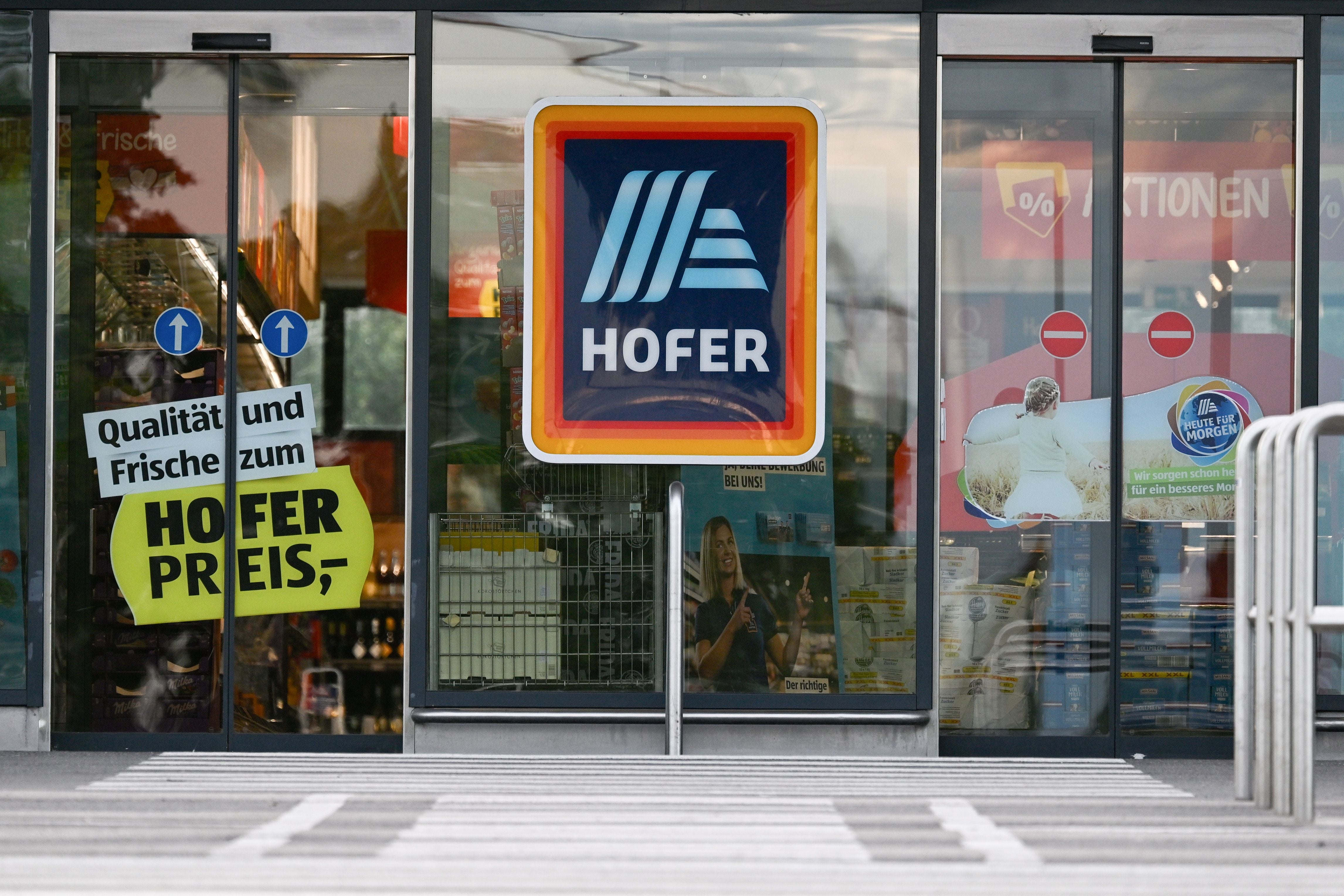 Eingang einer Hofer-Filiale mit großem Hofer-Logo und Werbeschildern an der Tür.