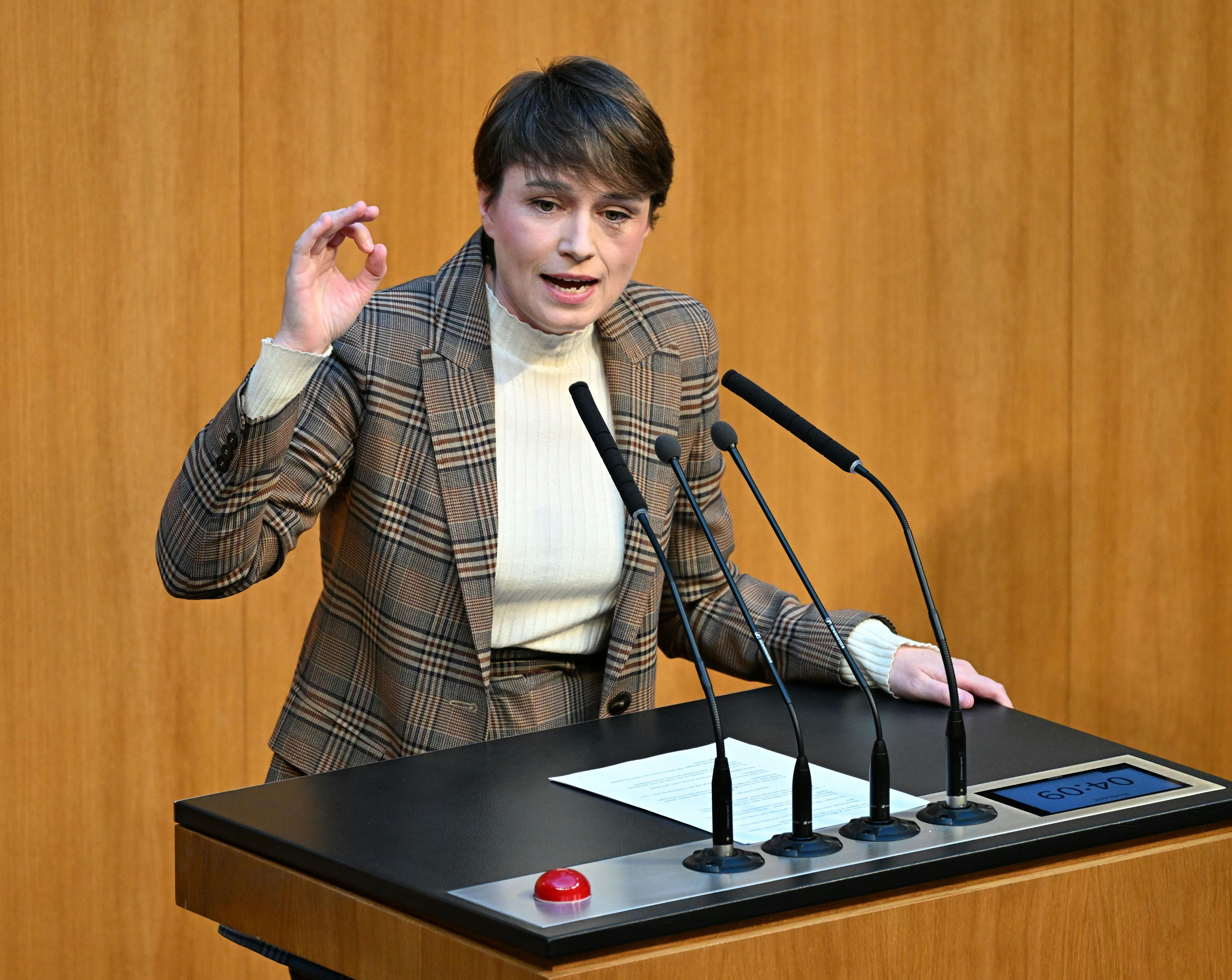Eine Frau spricht gestikulierend an einem Rednerpult im Parlament vor drei Mikrofonen.