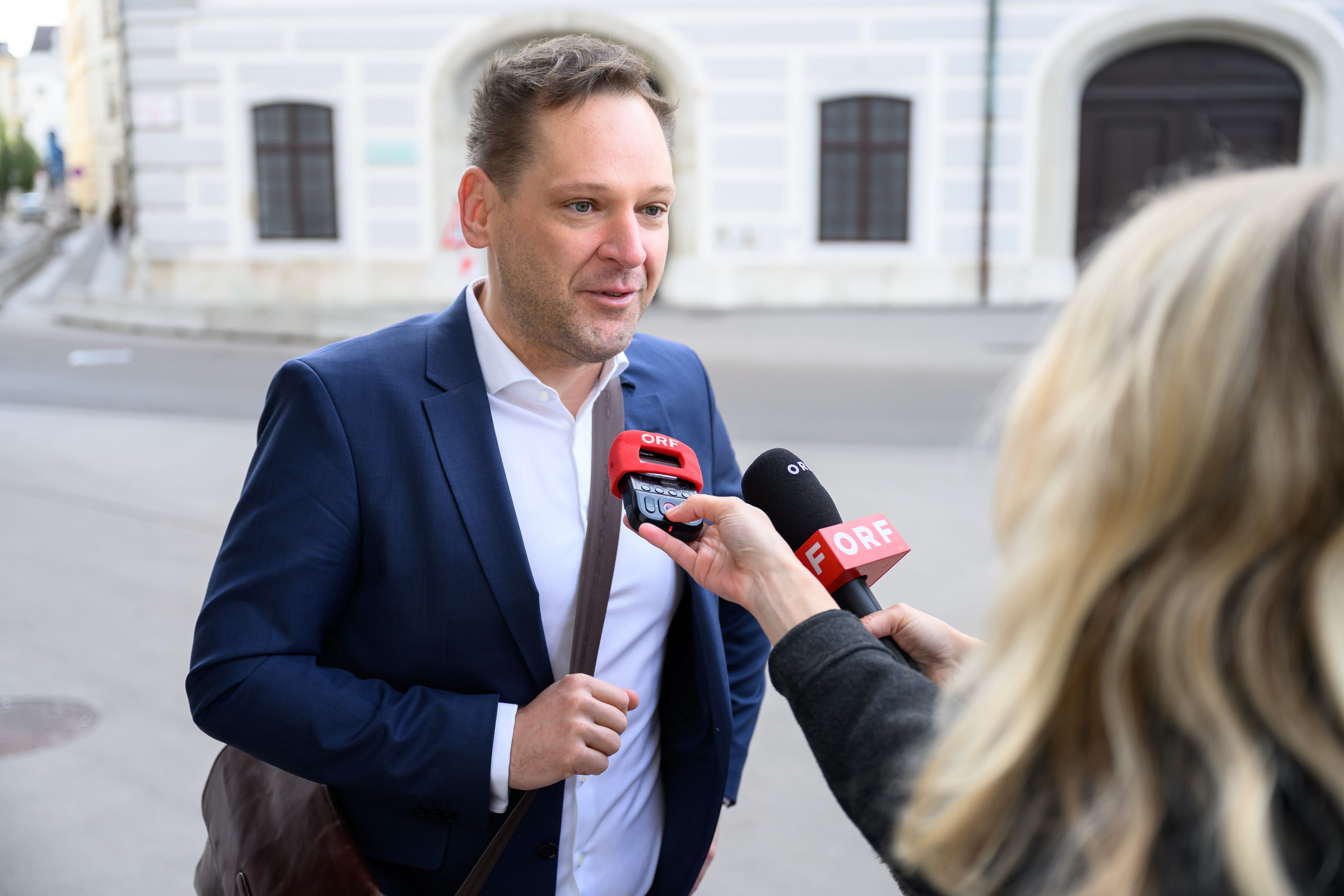 Ein Mann im Anzug wird auf der Straße von Journalisten mit ORF-Mikrofonen interviewt.