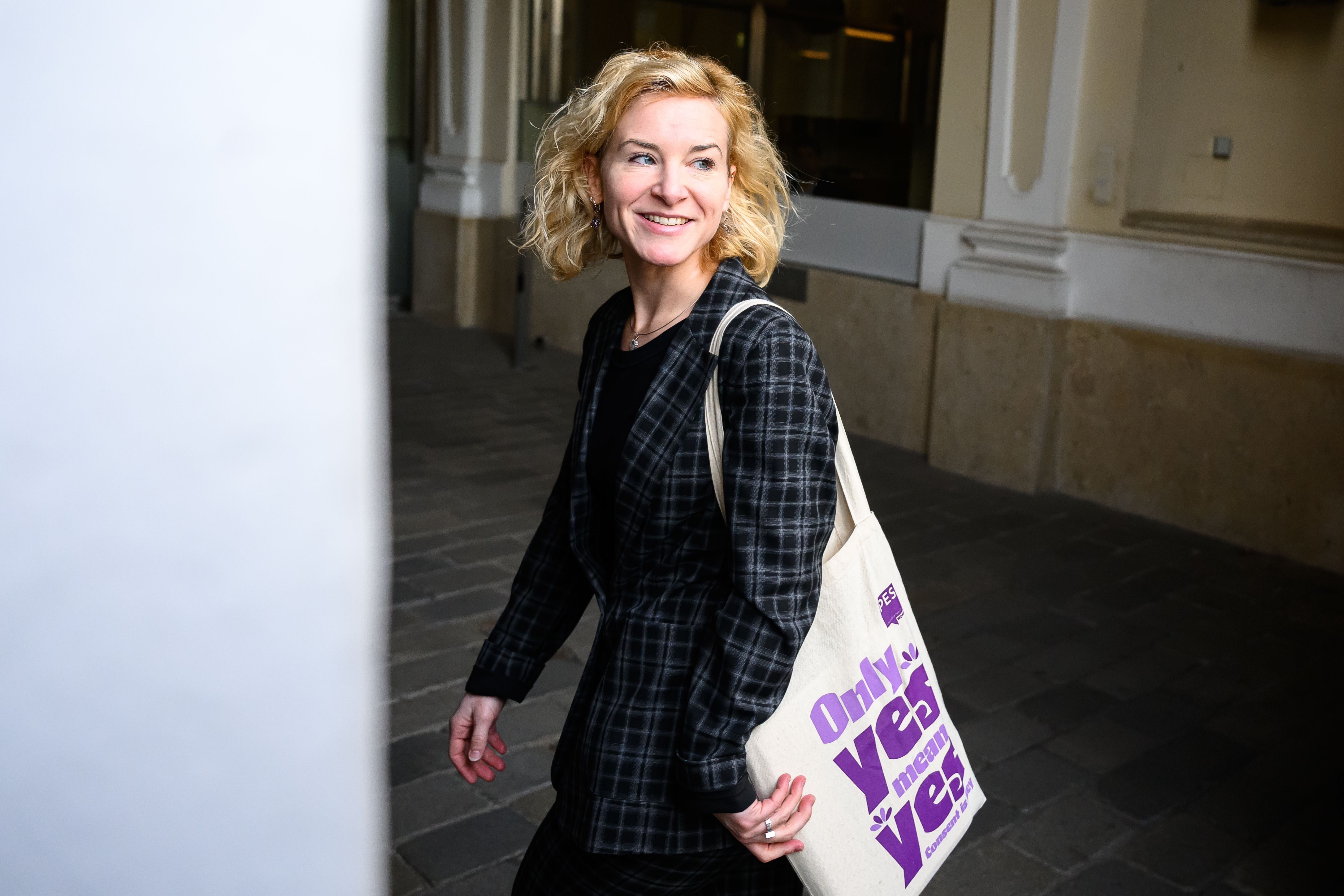 Frau mit kariertem Anzug und Stofftasche mit der Aufschrift „Only yes means yes“ geht lächelnd.
