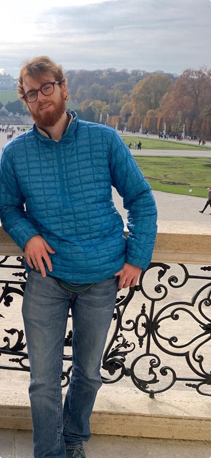 Mann mit Brille und blauer Jacke lehnt an einem verzierten Geländer im Freien.