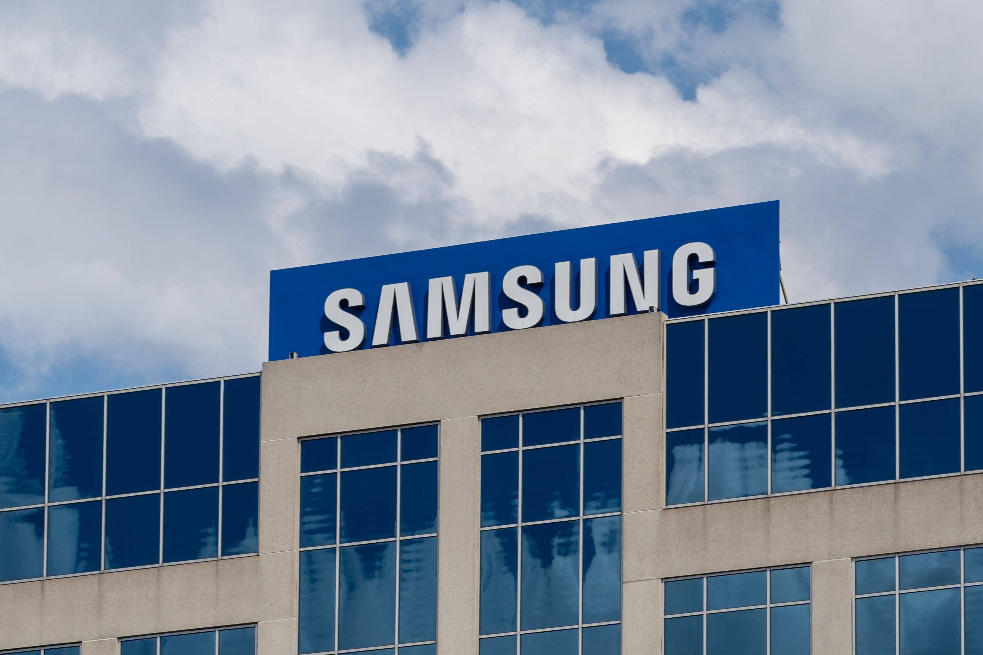 Samsung-Logo auf einem modernen Bürogebäude vor bewölktem Himmel.