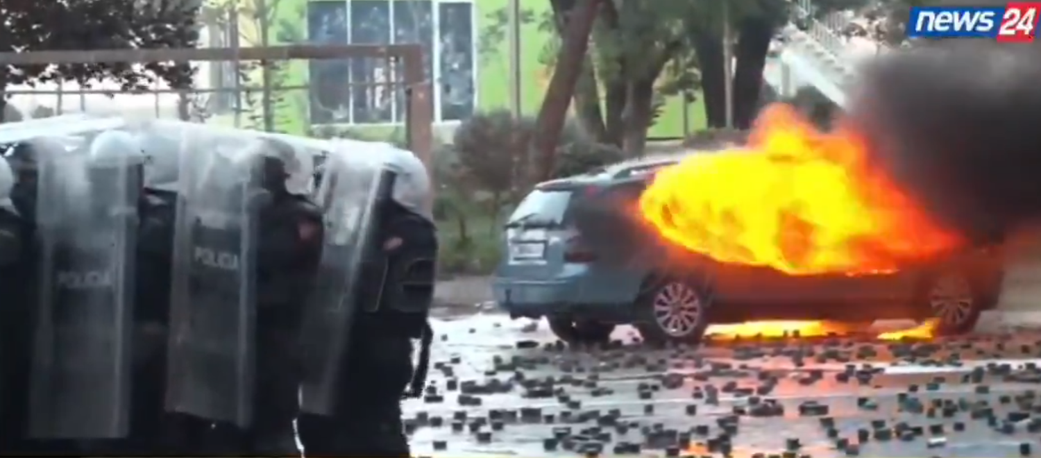 Polizisten mit Schilden stehen neben einem brennenden Auto bei Protesten in Albanien.
