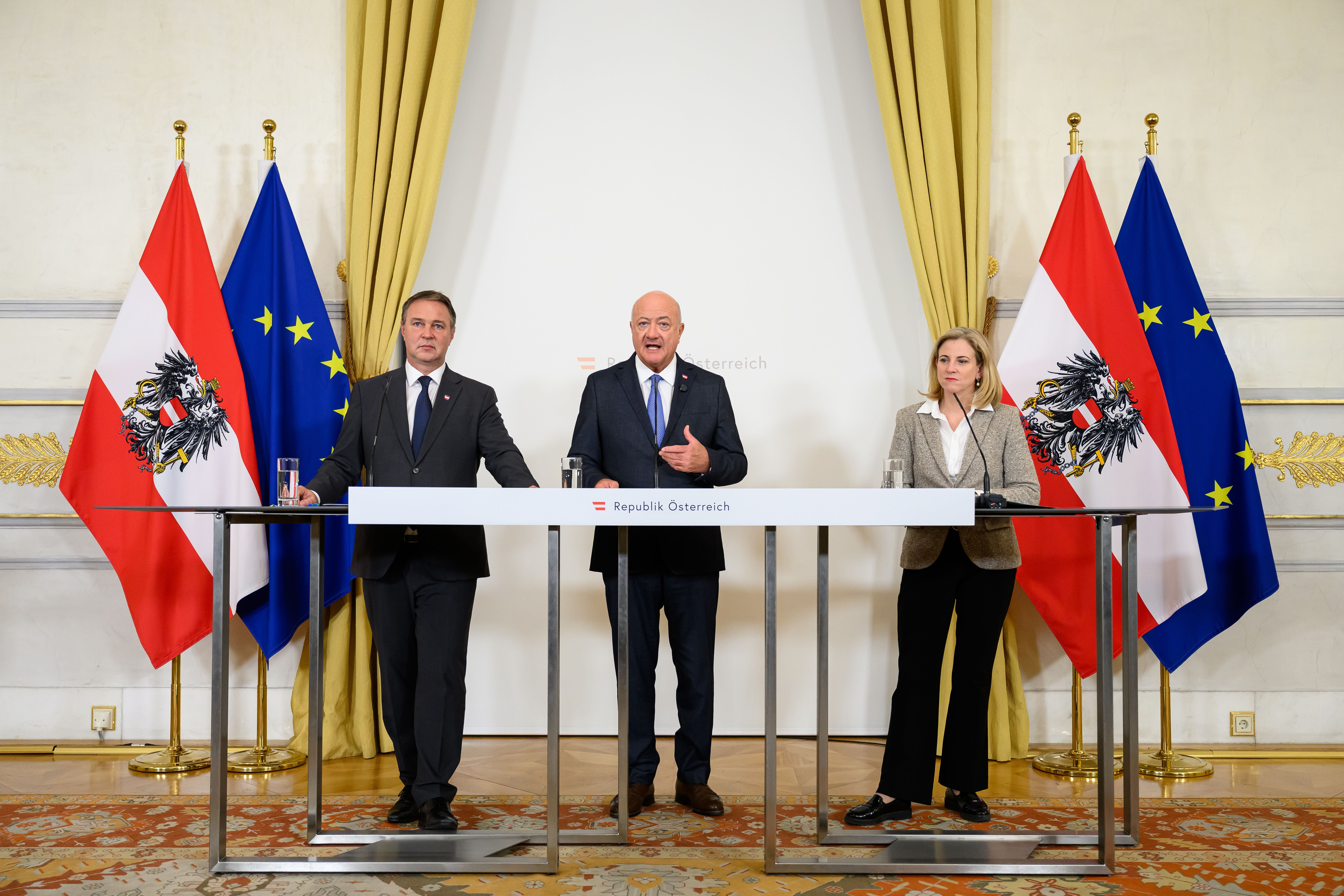Drei Politiker stehen bei einer Pressekonferenz vor österreichischen und EU-Flaggen in Wien.