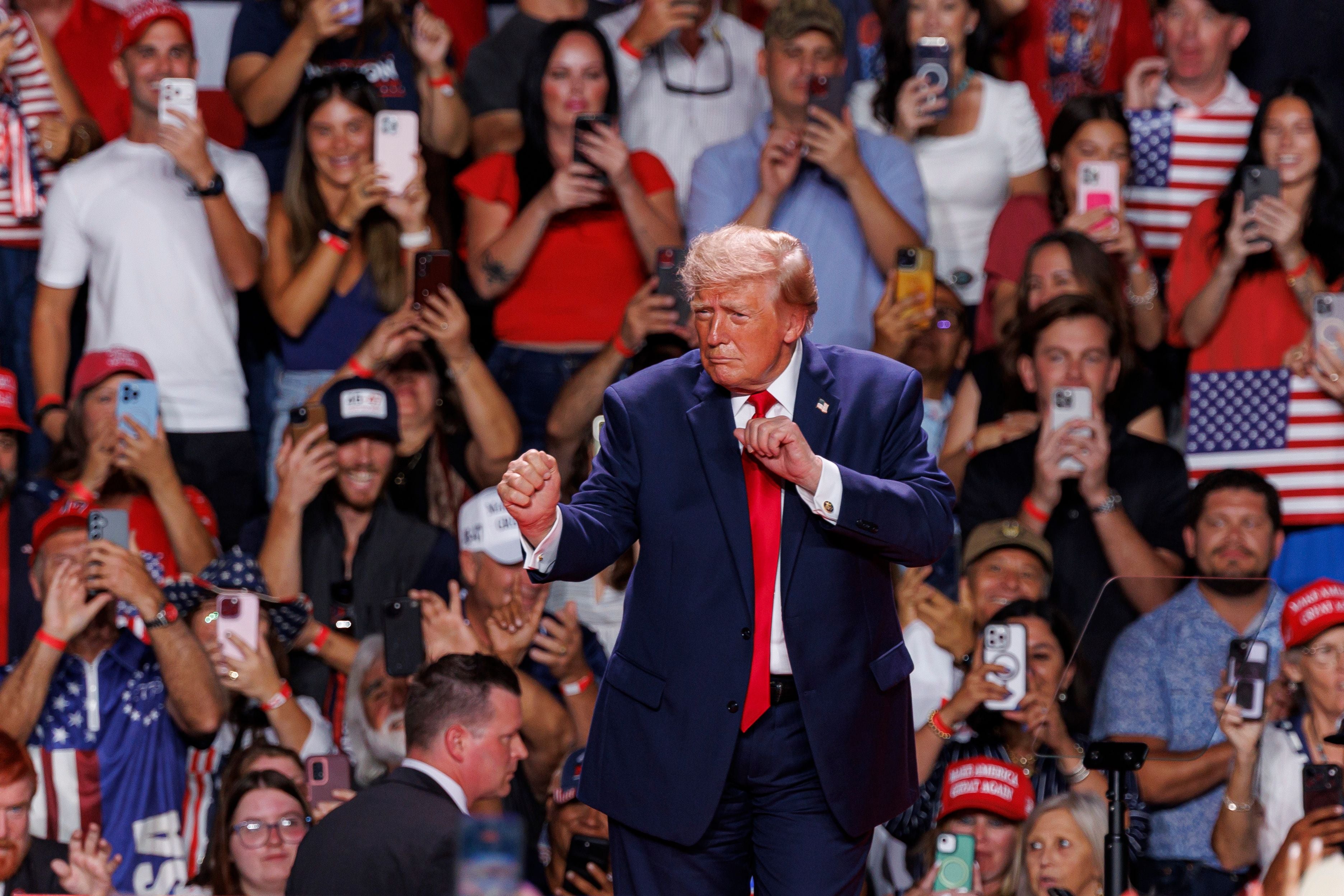 Donald Trump tanzt auf einer Bühne vor jubelndem Publikum mit vielen amerikanischen Flaggen.