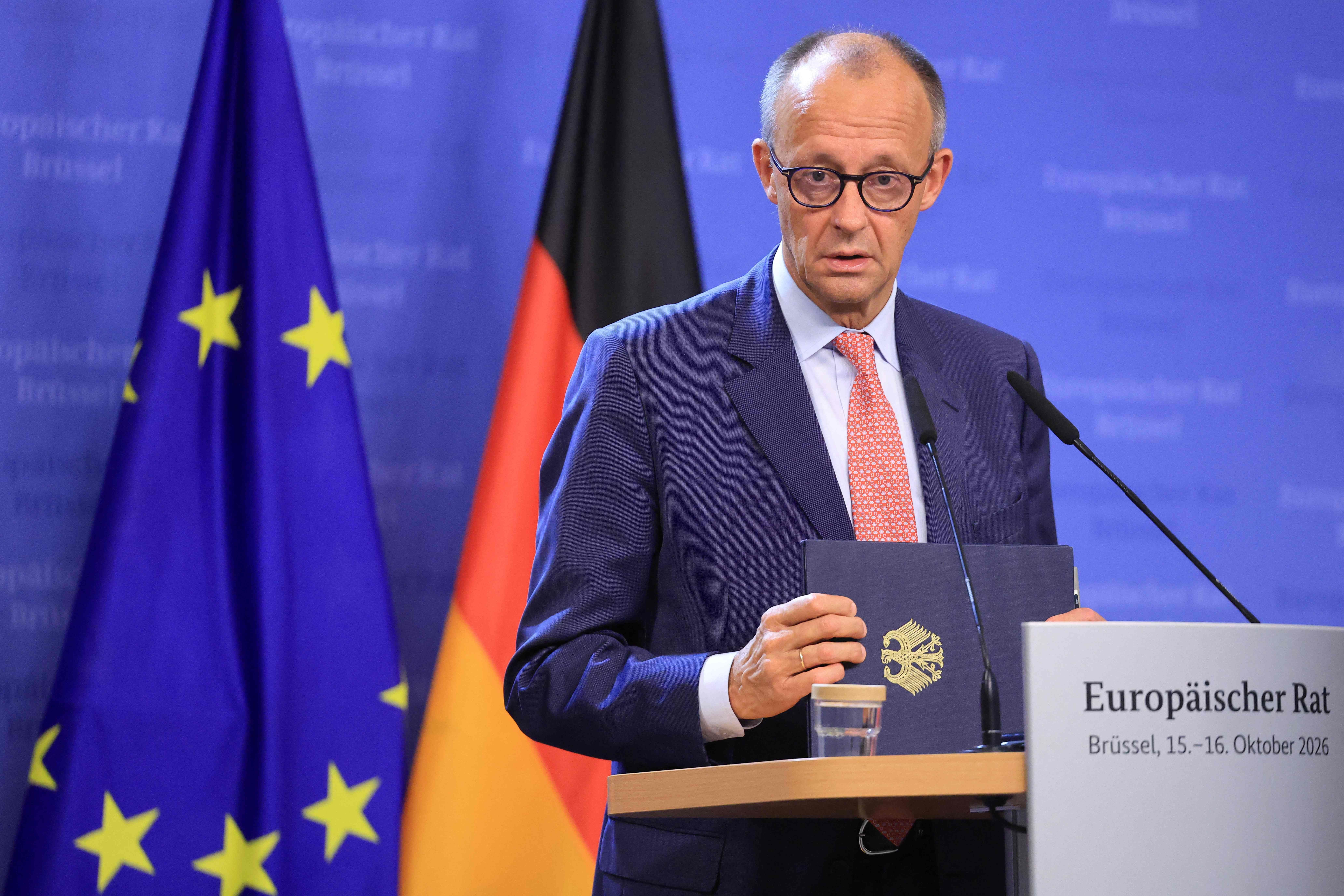Ein Mann hält eine Mappe bei einer Pressekonferenz vor EU- und Deutschlandflaggen in Brüssel.