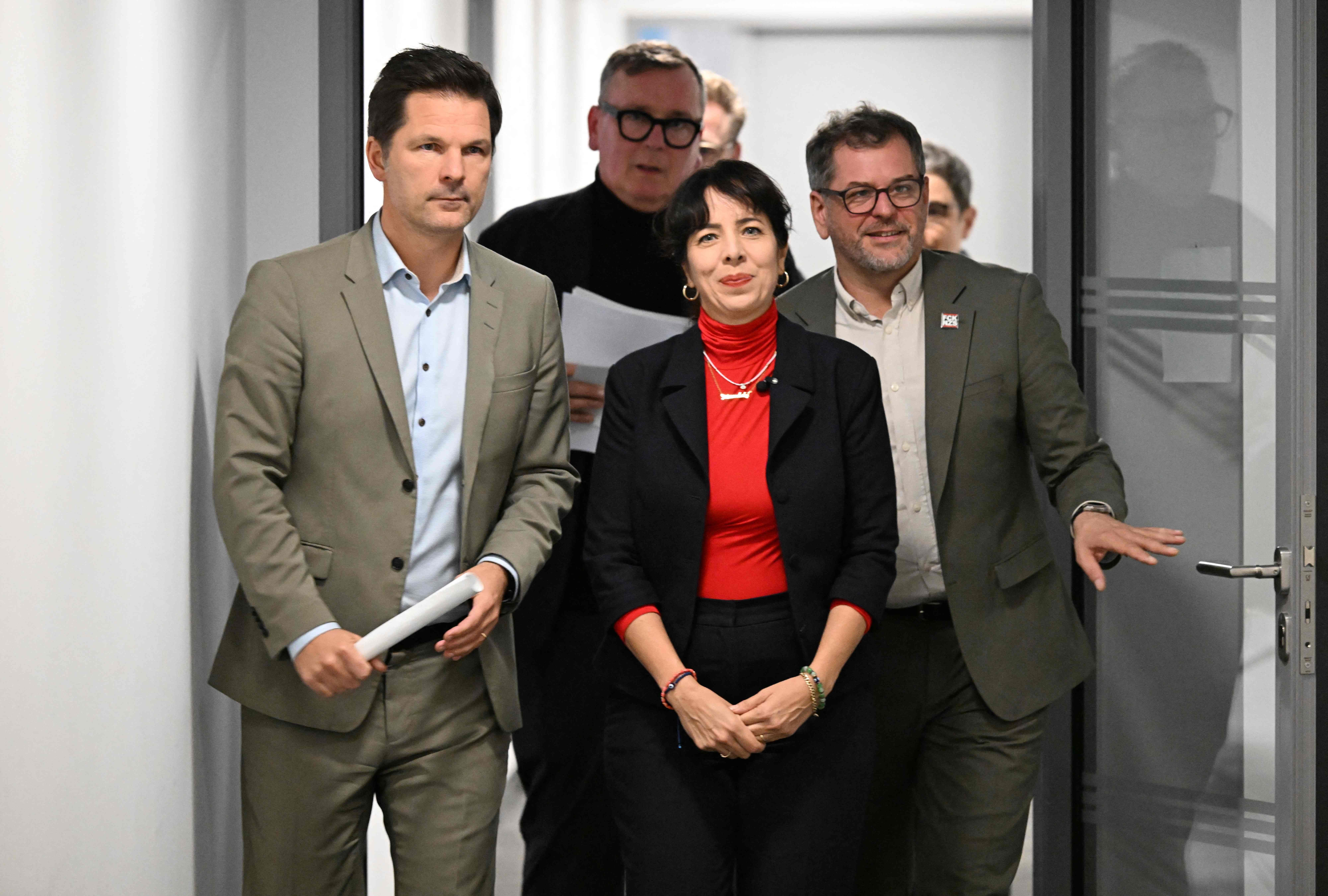 Drei Politiker gehen gemeinsam einen Flur entlang zu einer Pressekonferenz.