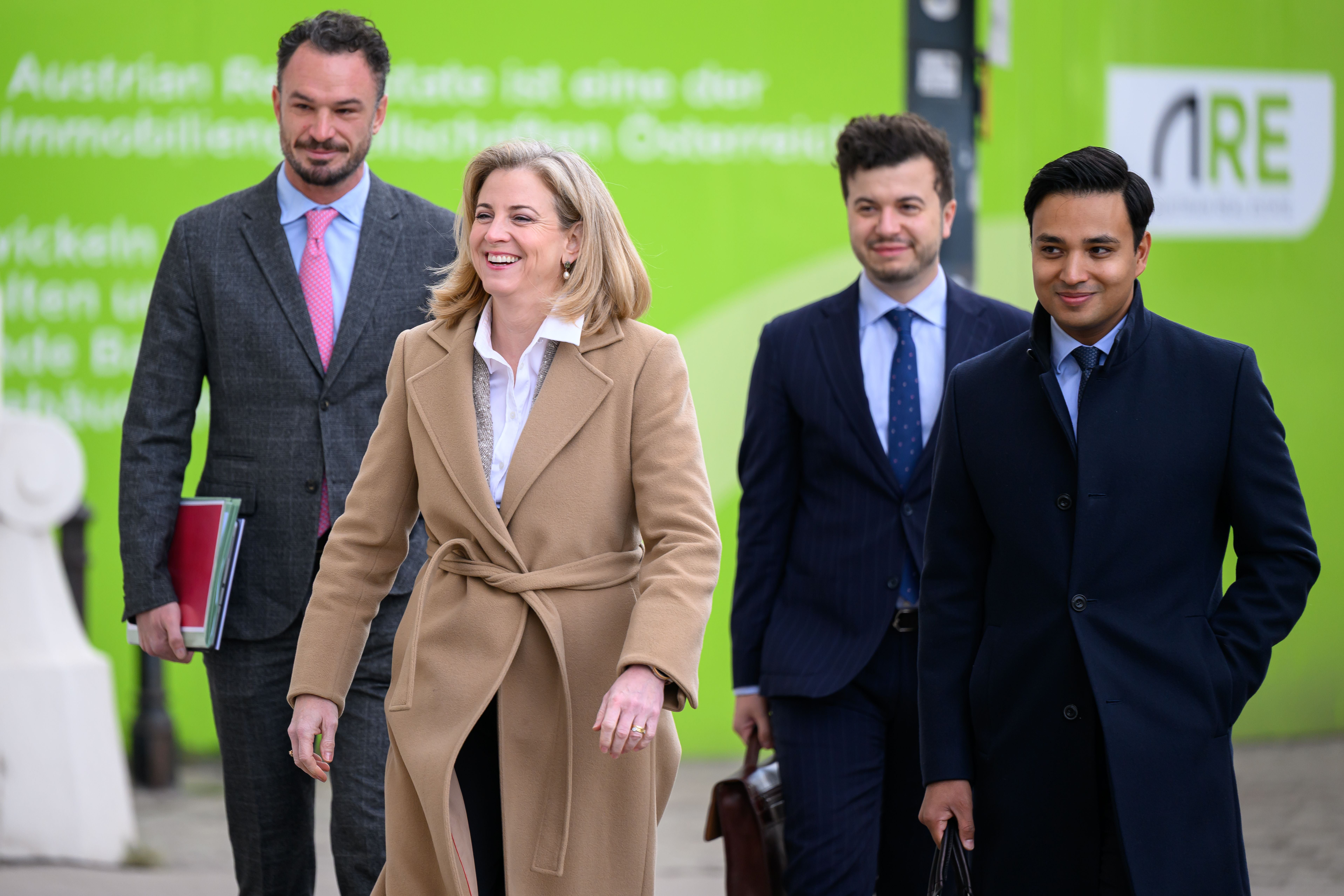Vier elegant gekleidete Personen gehen lächelnd nebeneinander auf einer Straße.