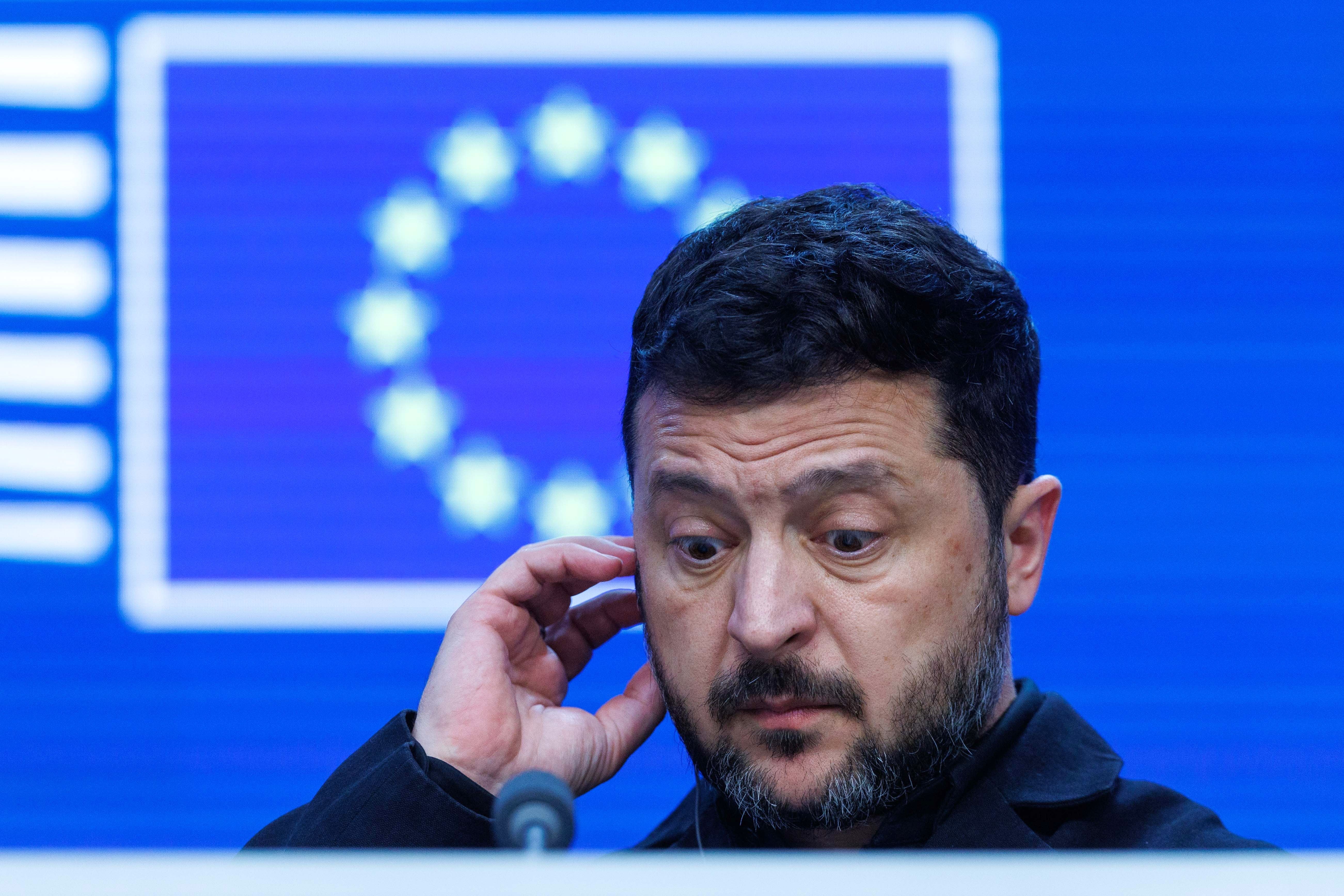 Ein Mann steht nachdenklich vor einem Mikrofon, im Hintergrund eine unscharfe EU-Flagge.