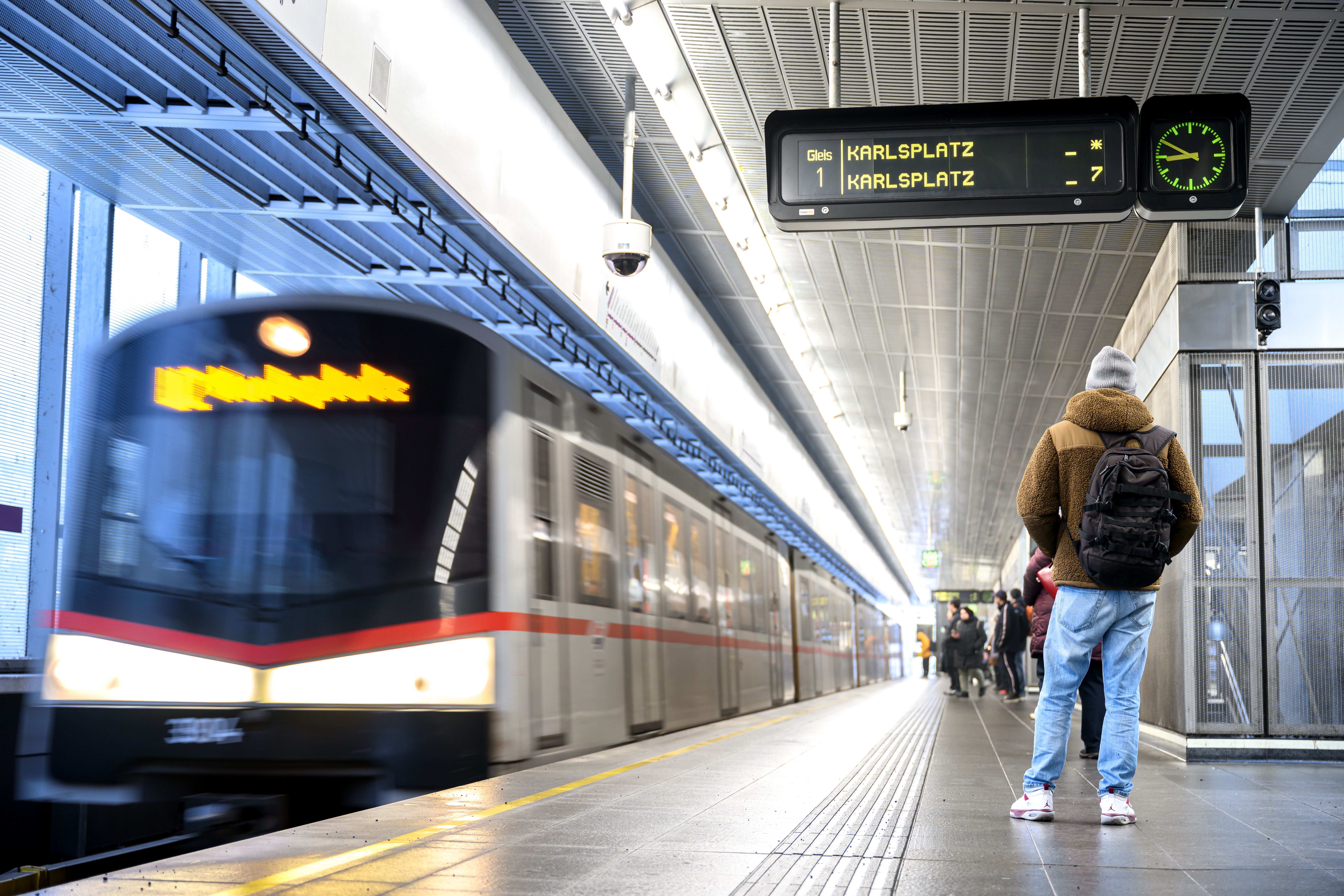 Eine Person wartet am Wiener U-Bahnsteig, während eine U-Bahn in die Station einfährt.