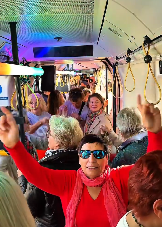 Mehrere ältere Menschen feiern und tanzen fröhlich in einer bunt beleuchteten Straßenbahn.