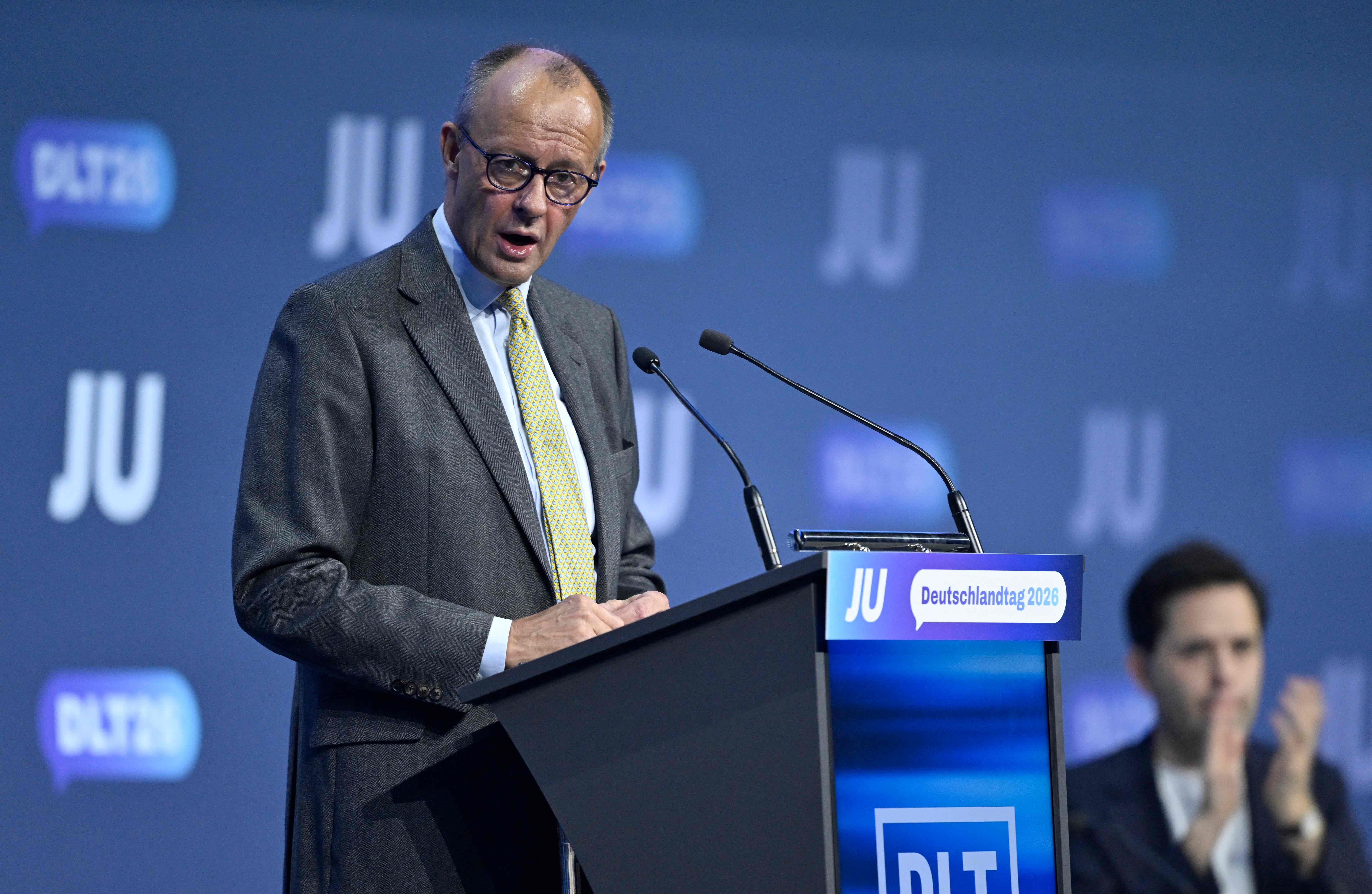 Ein Mann hält eine Rede am Rednerpult beim Deutschlandtag der Jungen Union, daneben klatscht ein Zuhörer.