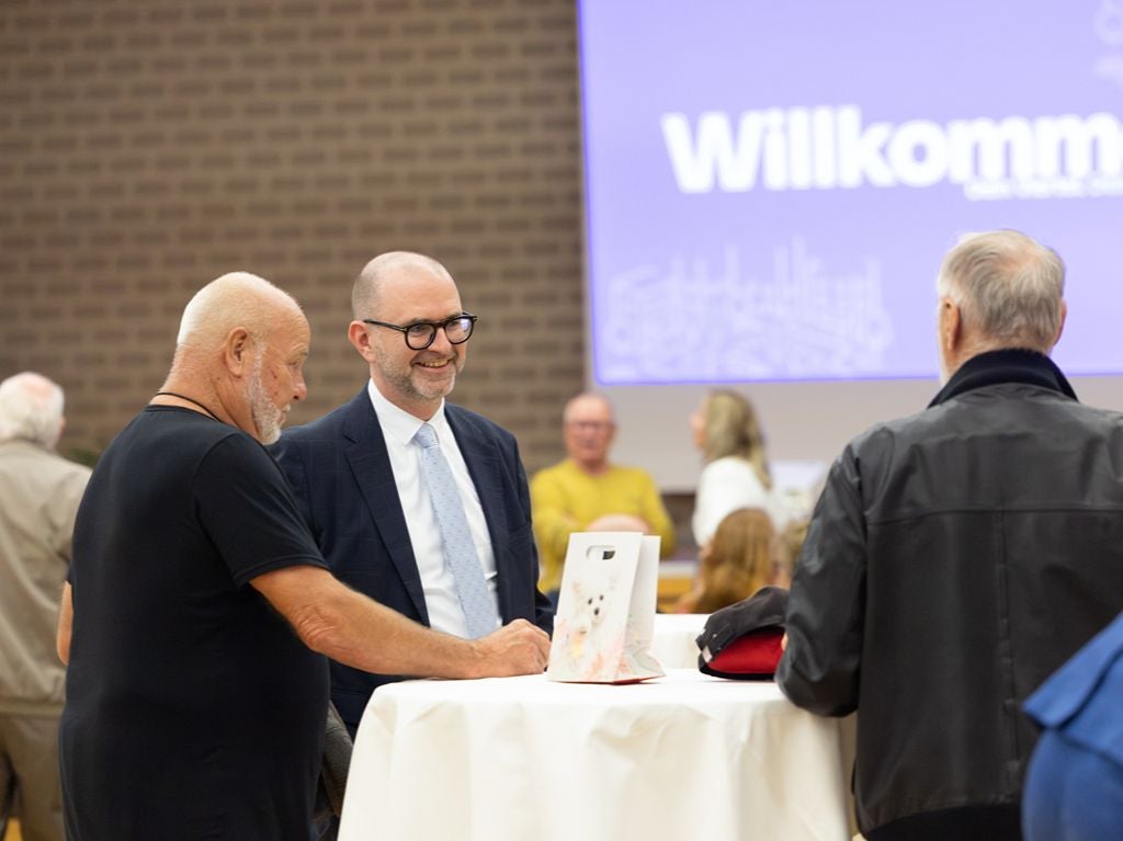 Bürgermeister spricht mit Bürgern an einem Stehtisch bei einer Willkommensveranstaltung.