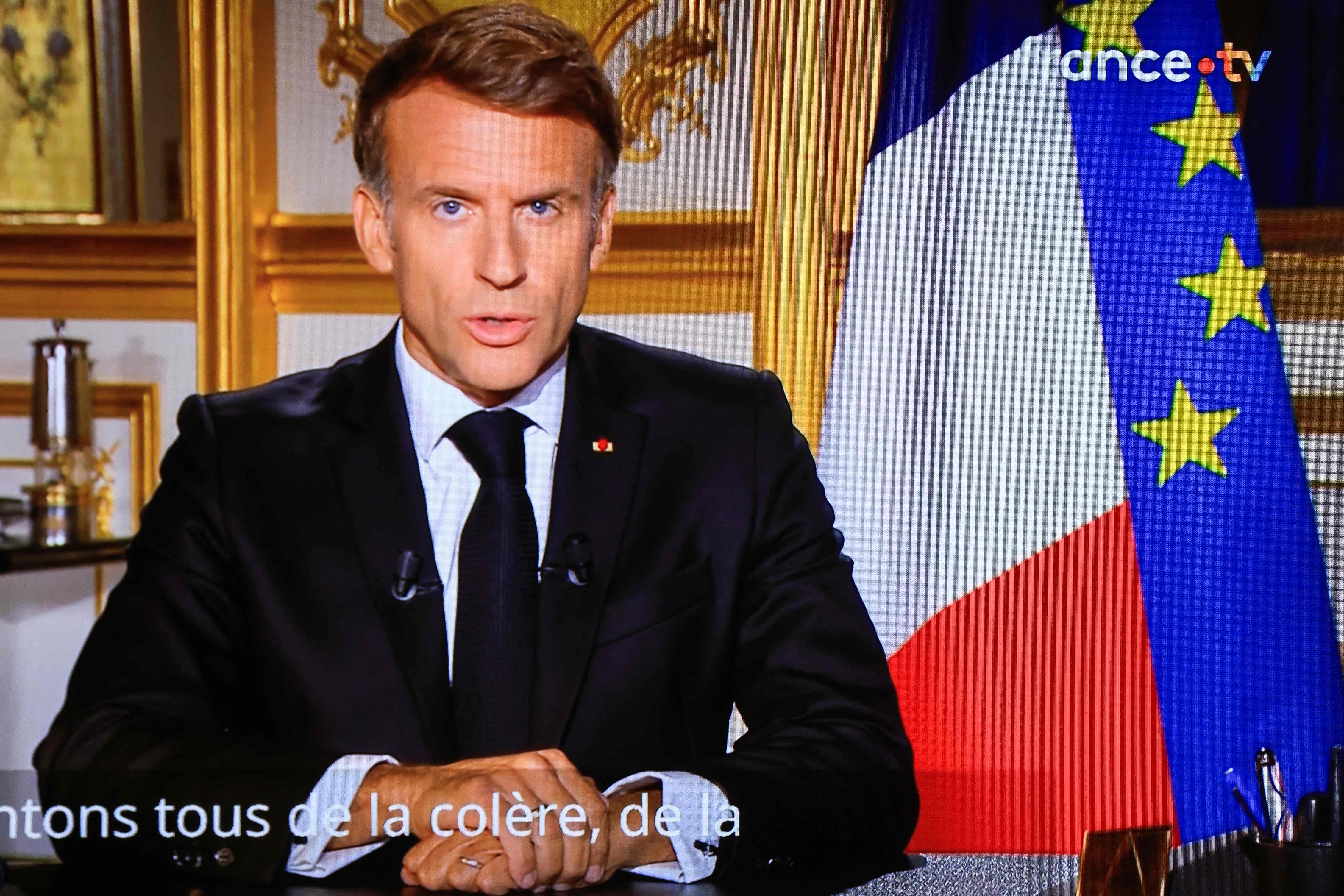 Emmanuel Macron hält eine Fernsehansprache, hinter ihm französische und EU-Flagge.