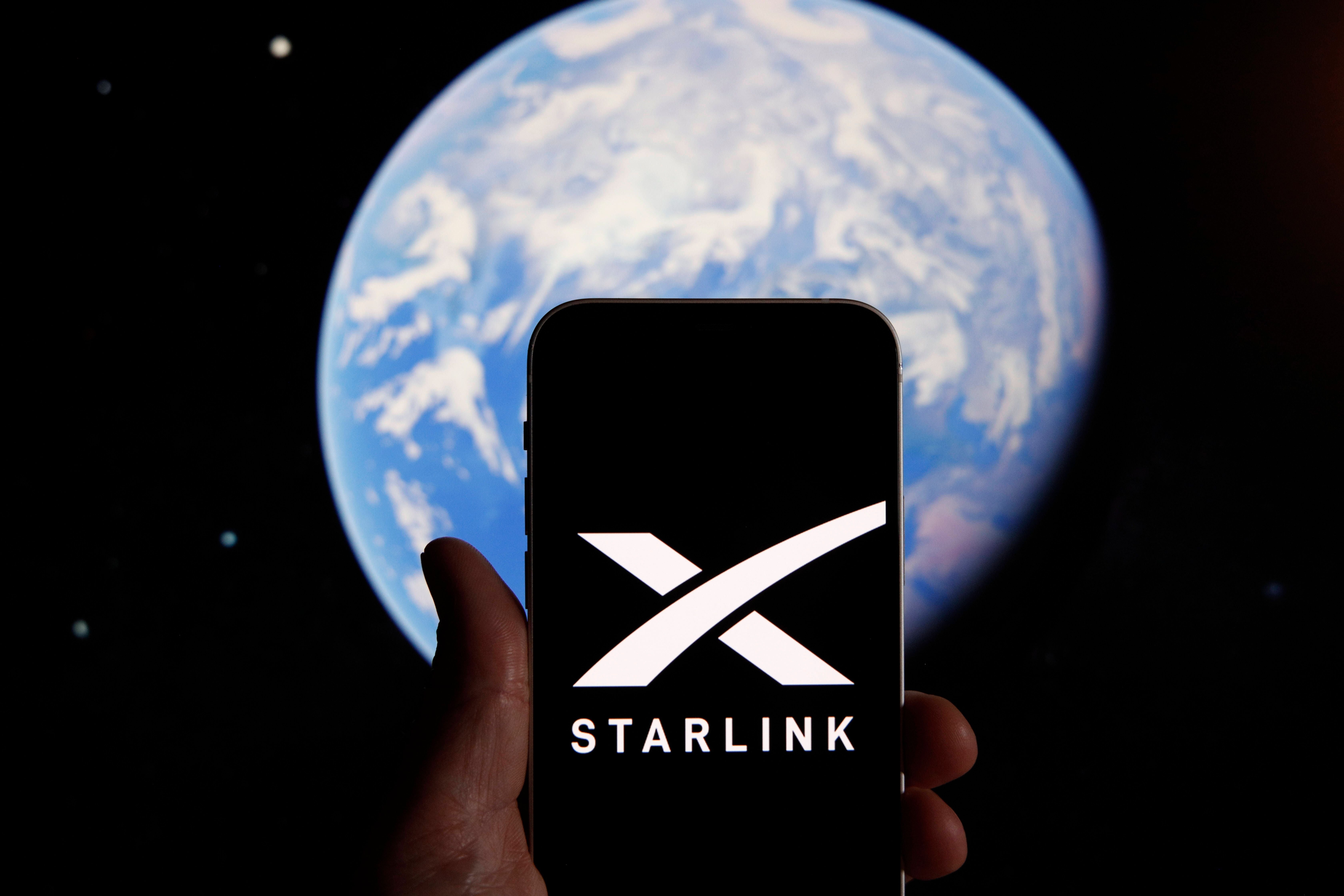 Hand hält ein Smartphone mit Starlink-Logo vor einer grafischen Darstellung der Erde.