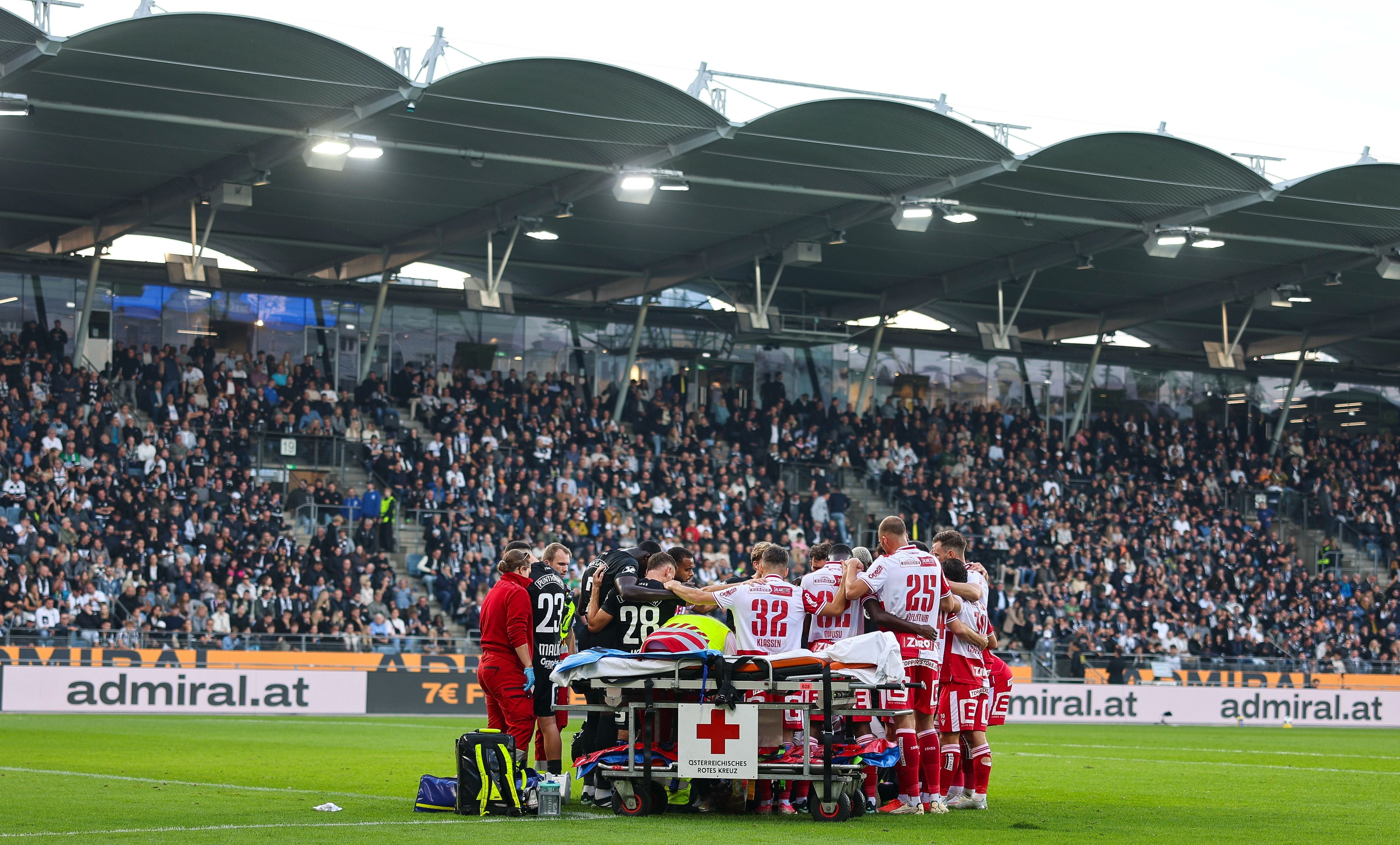 Spieler beider Teams bilden einen Sichtschutz um den schwer verletzten Sturm-Goalie Daniil Khudyakov, der unter dem Applaus der Fans abtransportiert wird.