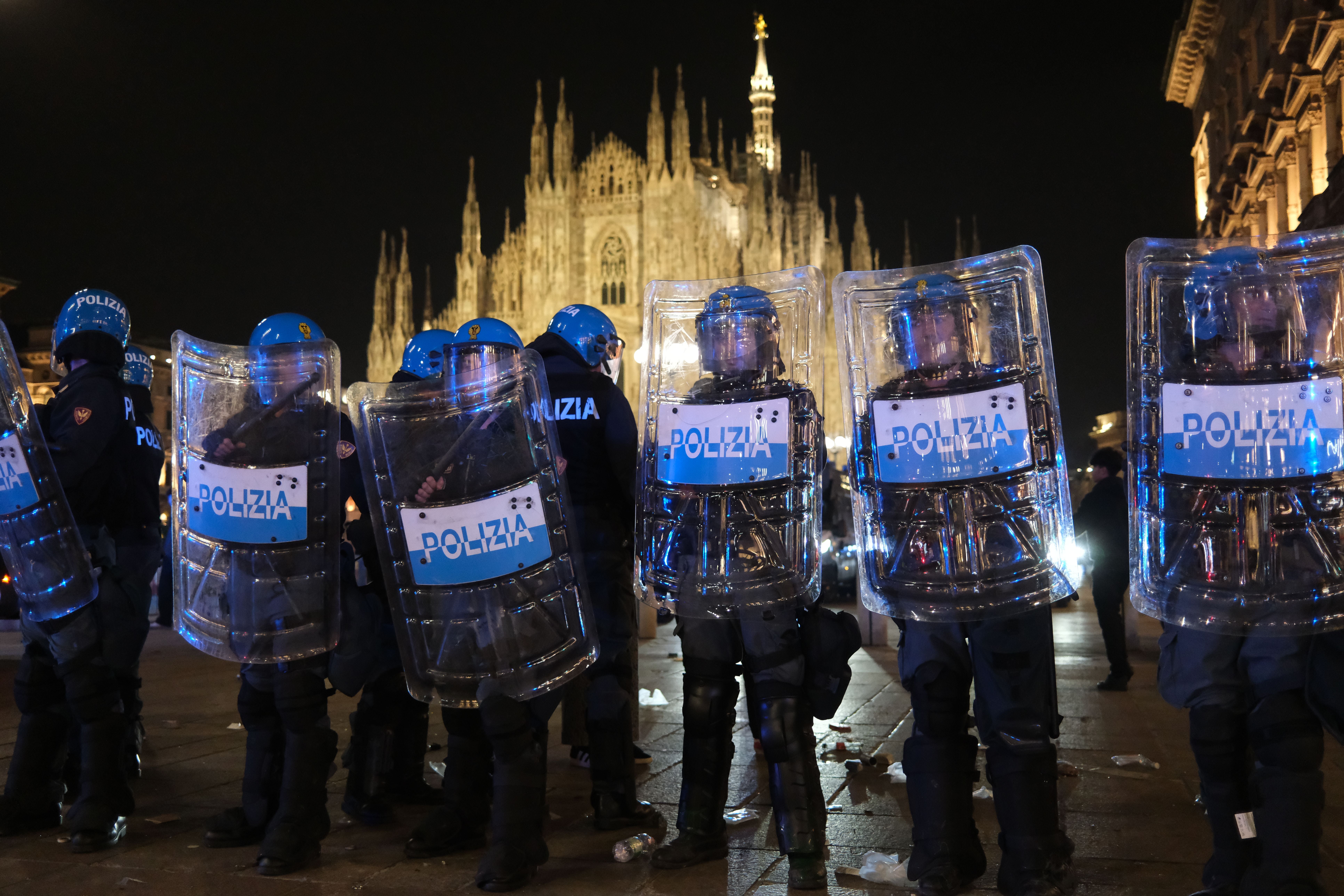 Polizisten mit Schilden stehen nachts vor dem Mailänder Dom auf einem Platz mit Müll am Boden.