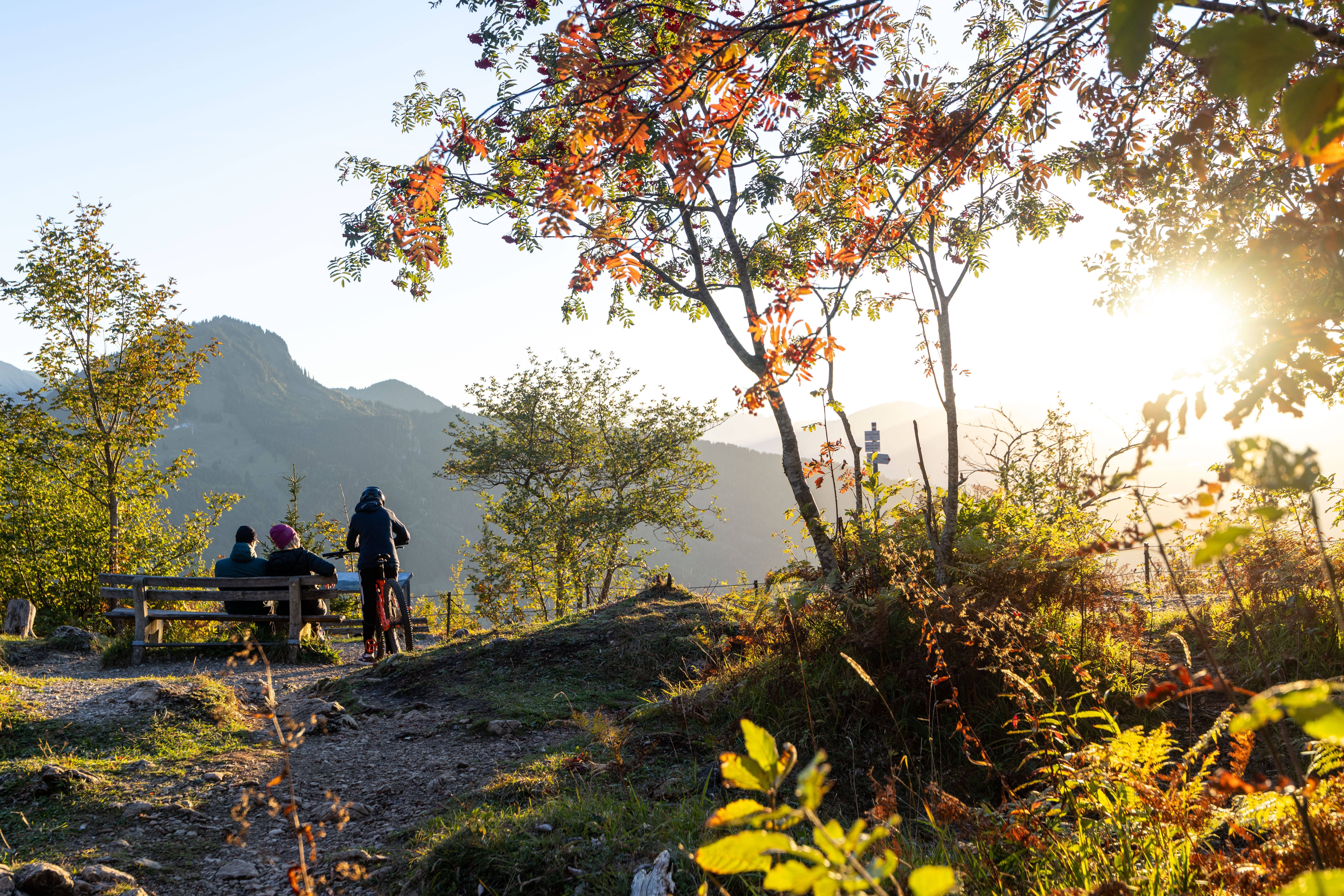 Drei Menschen genießen auf einer Bank einen sonnigen Herbstabend in den Allgäuer Alpen.