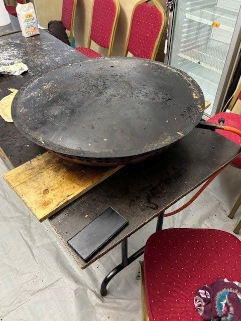 Große, runde Metallplatte zum Backen auf einem Tisch, umgeben von roten Stühlen.