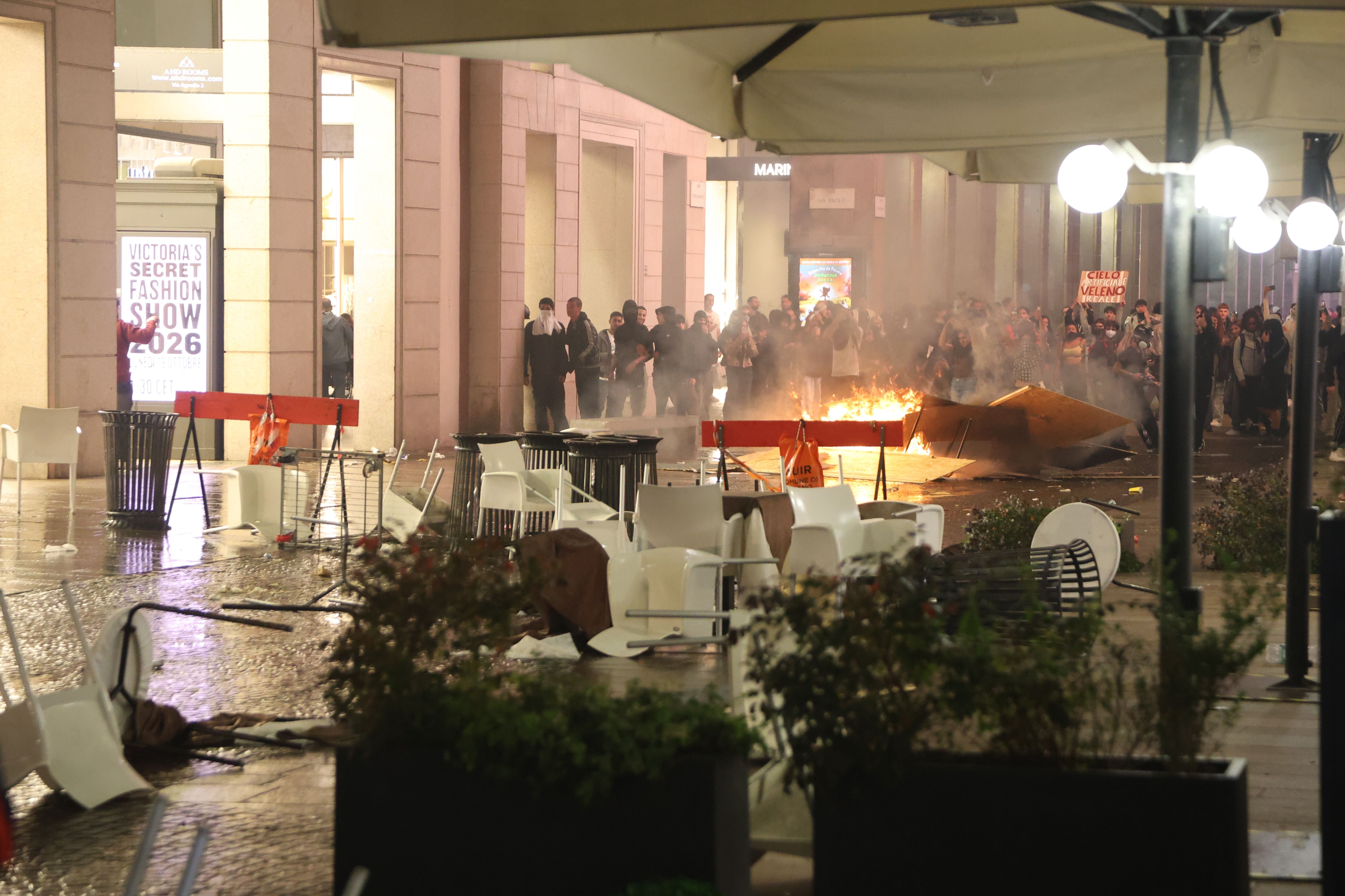 Umgestürzte Tische und brennende Barrikade bei einer Demonstration in einer Einkaufsstraße bei Nacht.