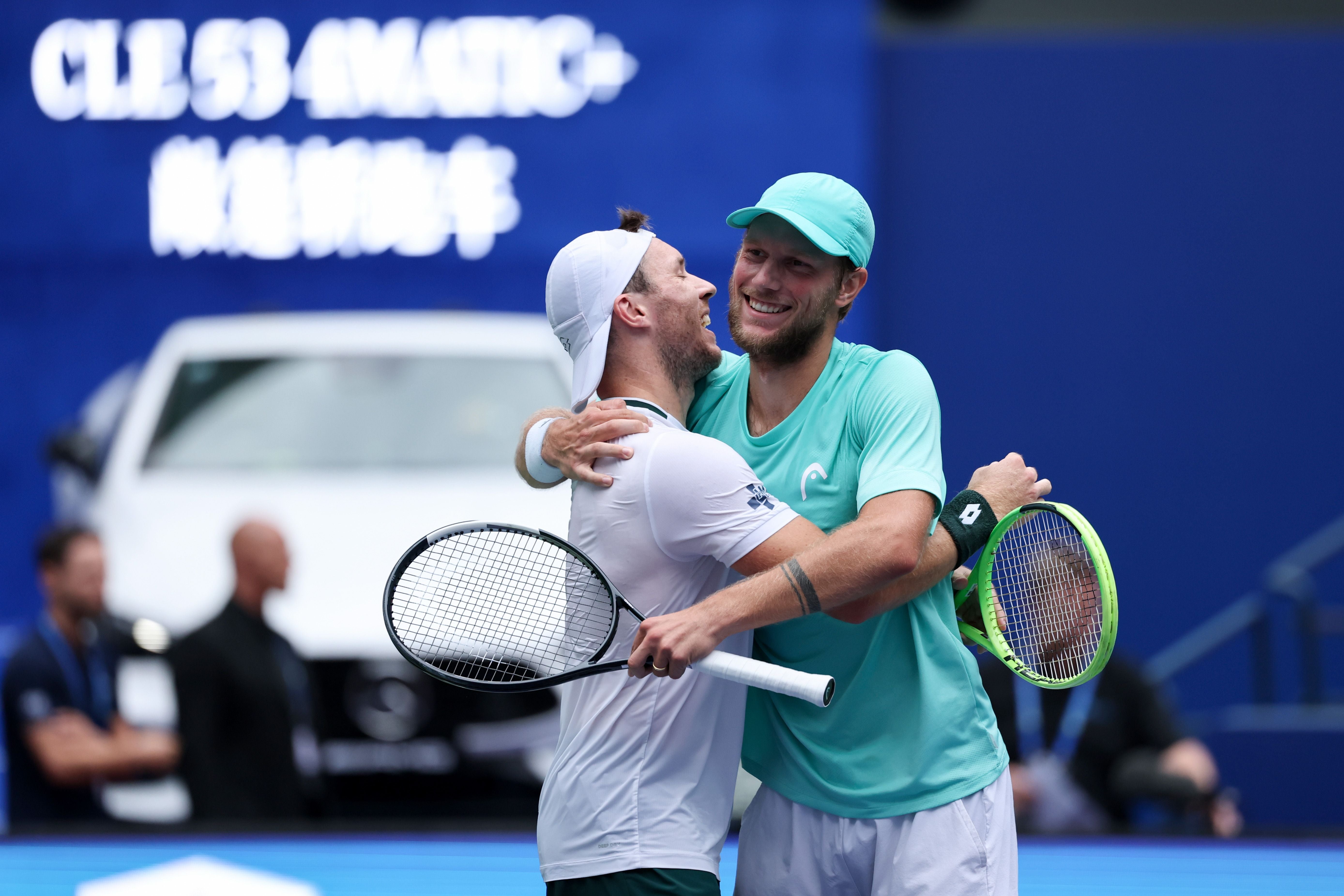 Zwei Tennisspieler umarmen sich jubelnd auf dem Platz nach einem Doppelsieg.