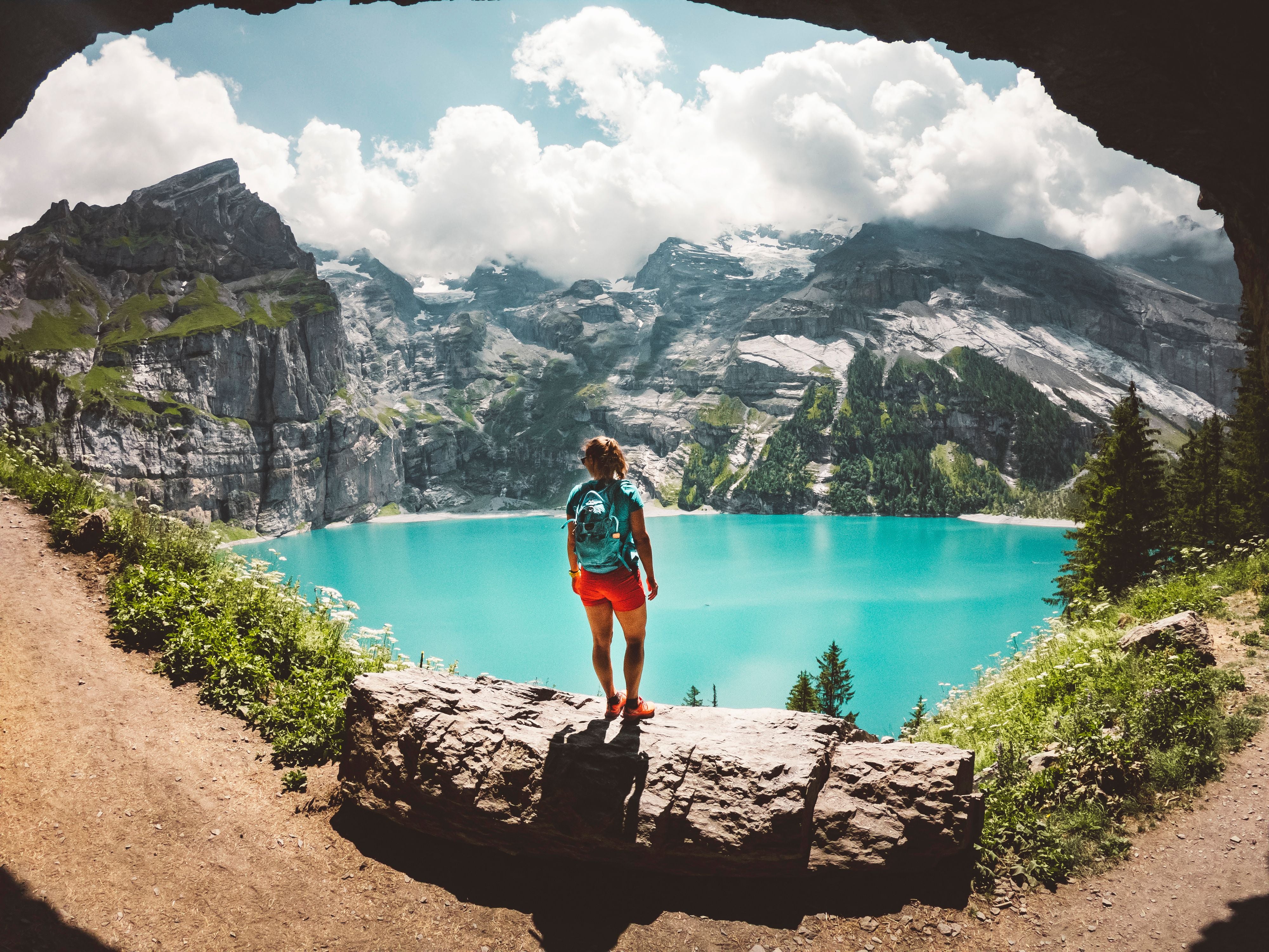 Wanderin steht vor einer Höhle mit Blick auf den türkisfarbenen Oeschinensee und Alpen.