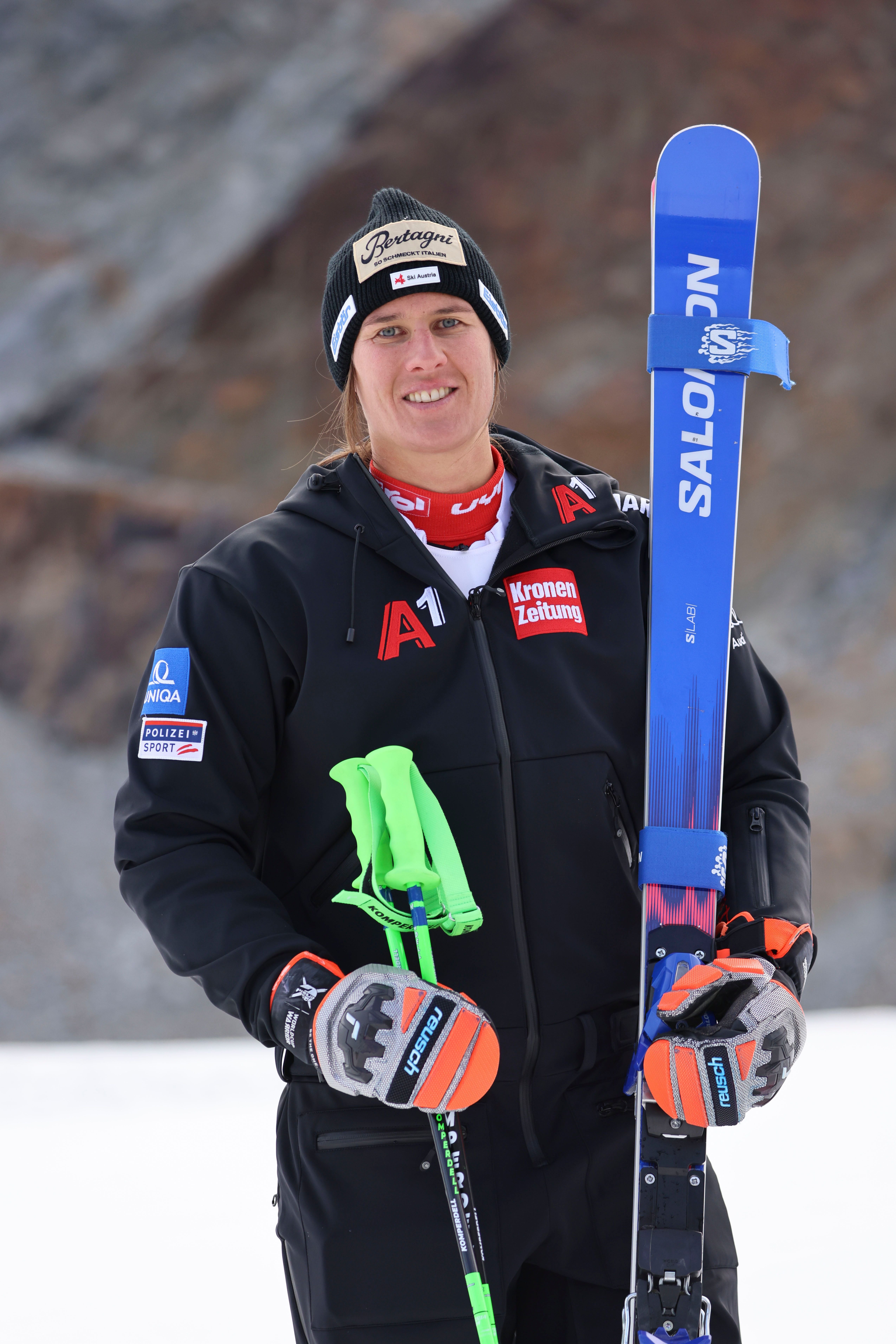 Eine Skifahrerin steht im Schnee mit Skiern und Skistöcken, trägt Winterkleidung und Mütze.