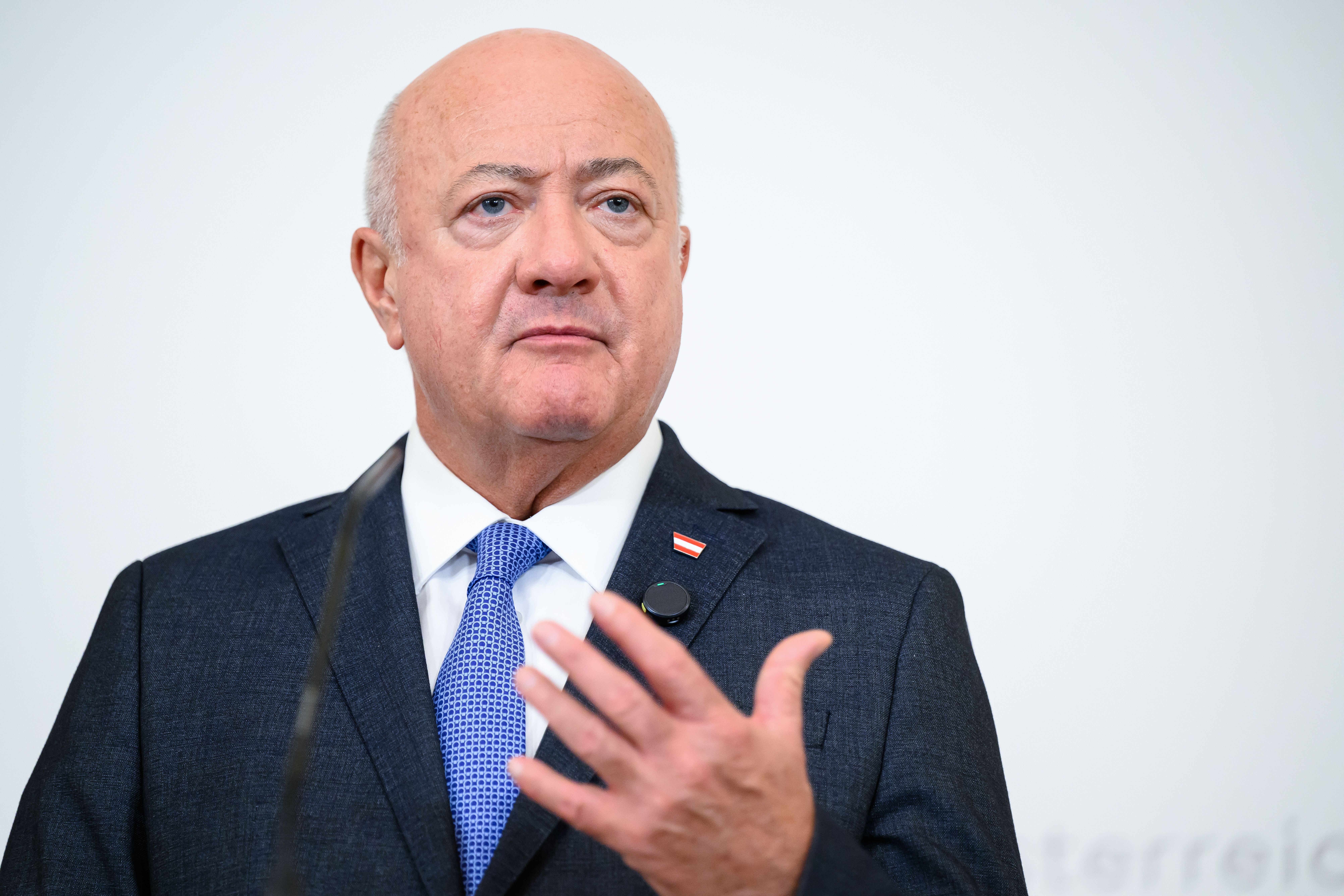 Ein Mann im Anzug spricht bei einer Pressekonferenz, ein Mikrofon ist sichtbar.