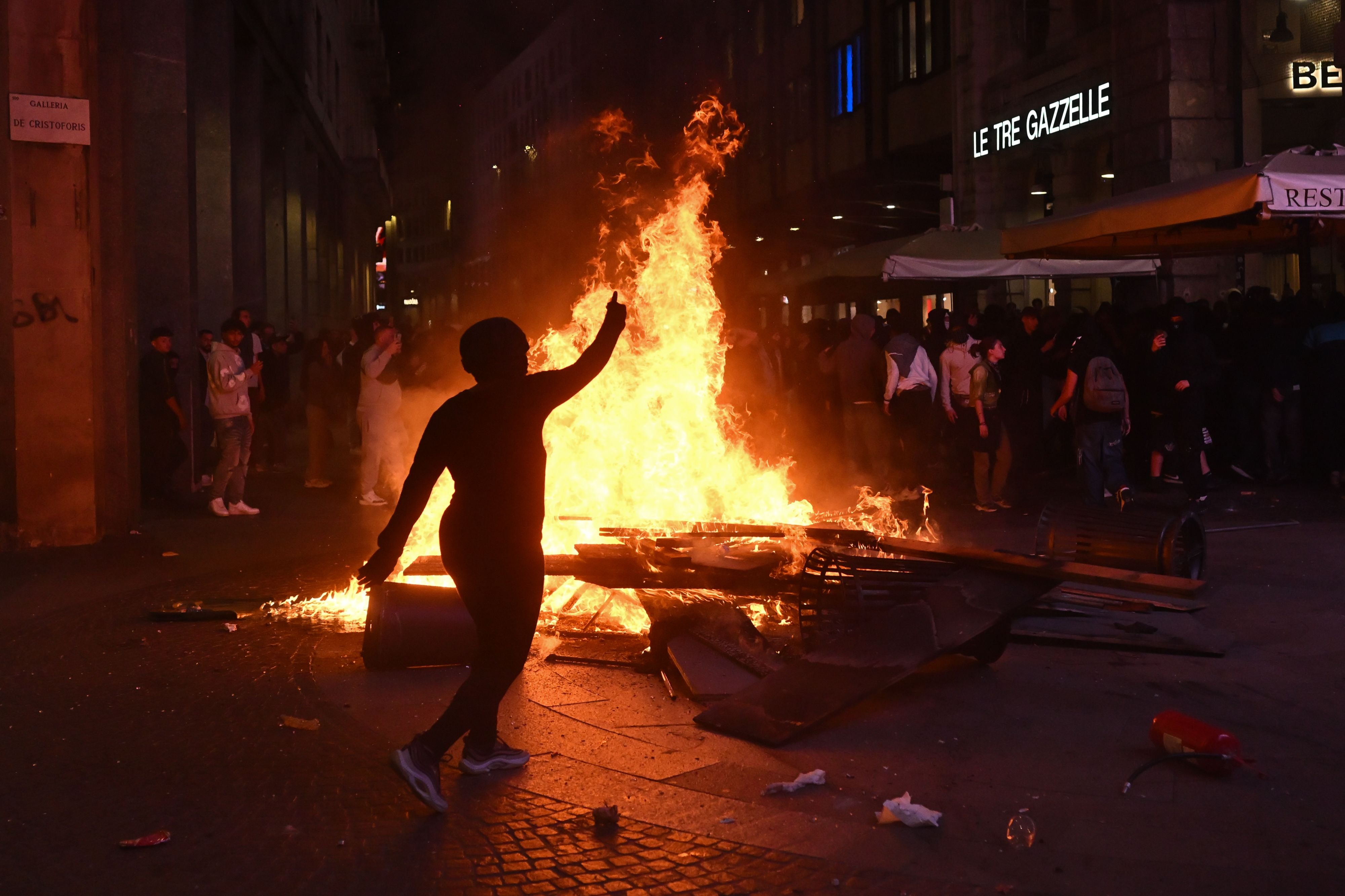 Eine brennende Barrikade bei Nacht, umgeben von Demonstrierenden auf einer Straße in Mailand.
