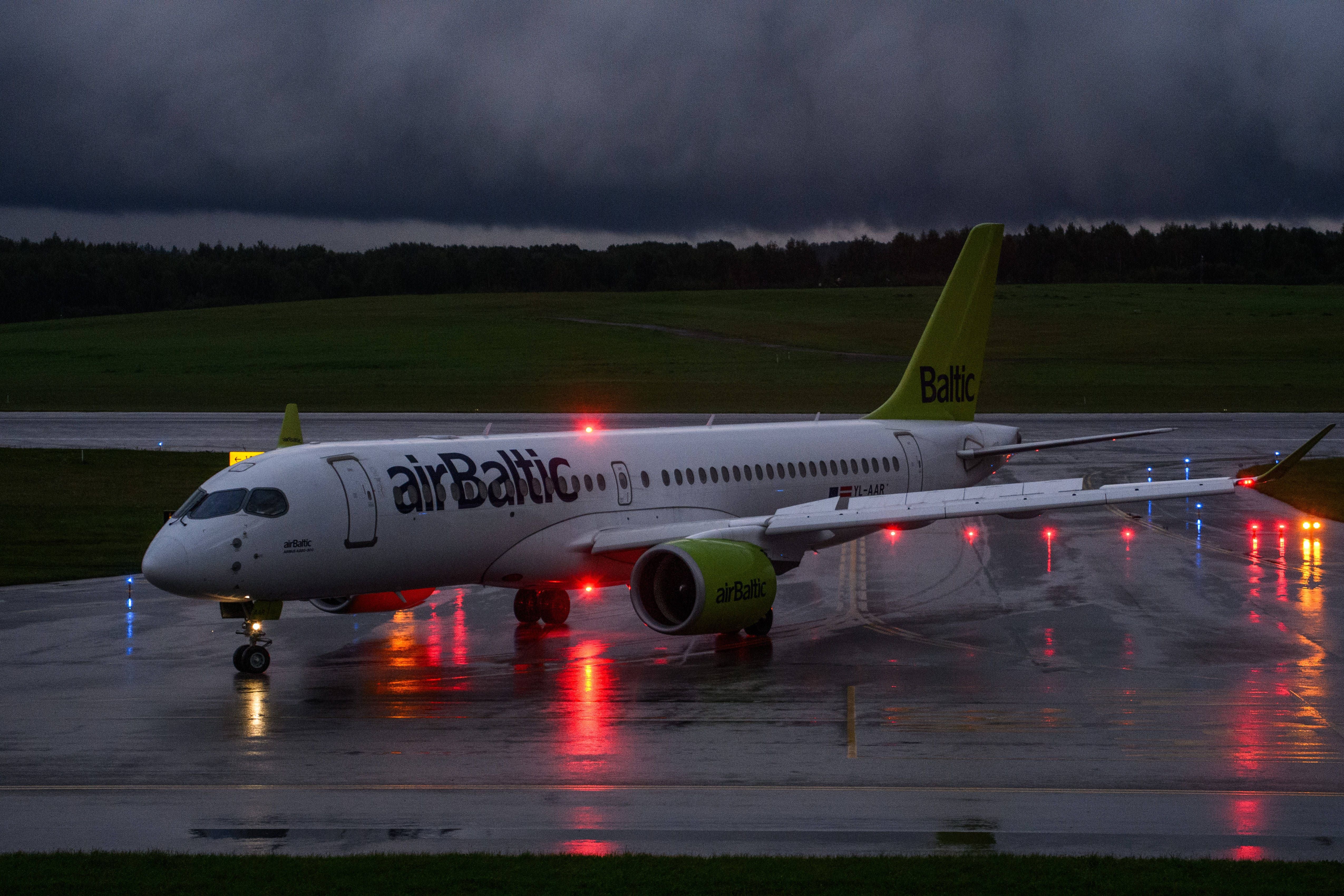 Ein Flugzeug von airBaltic steht bei Regen auf dem Rollfeld eines Flughafens bei Nacht.