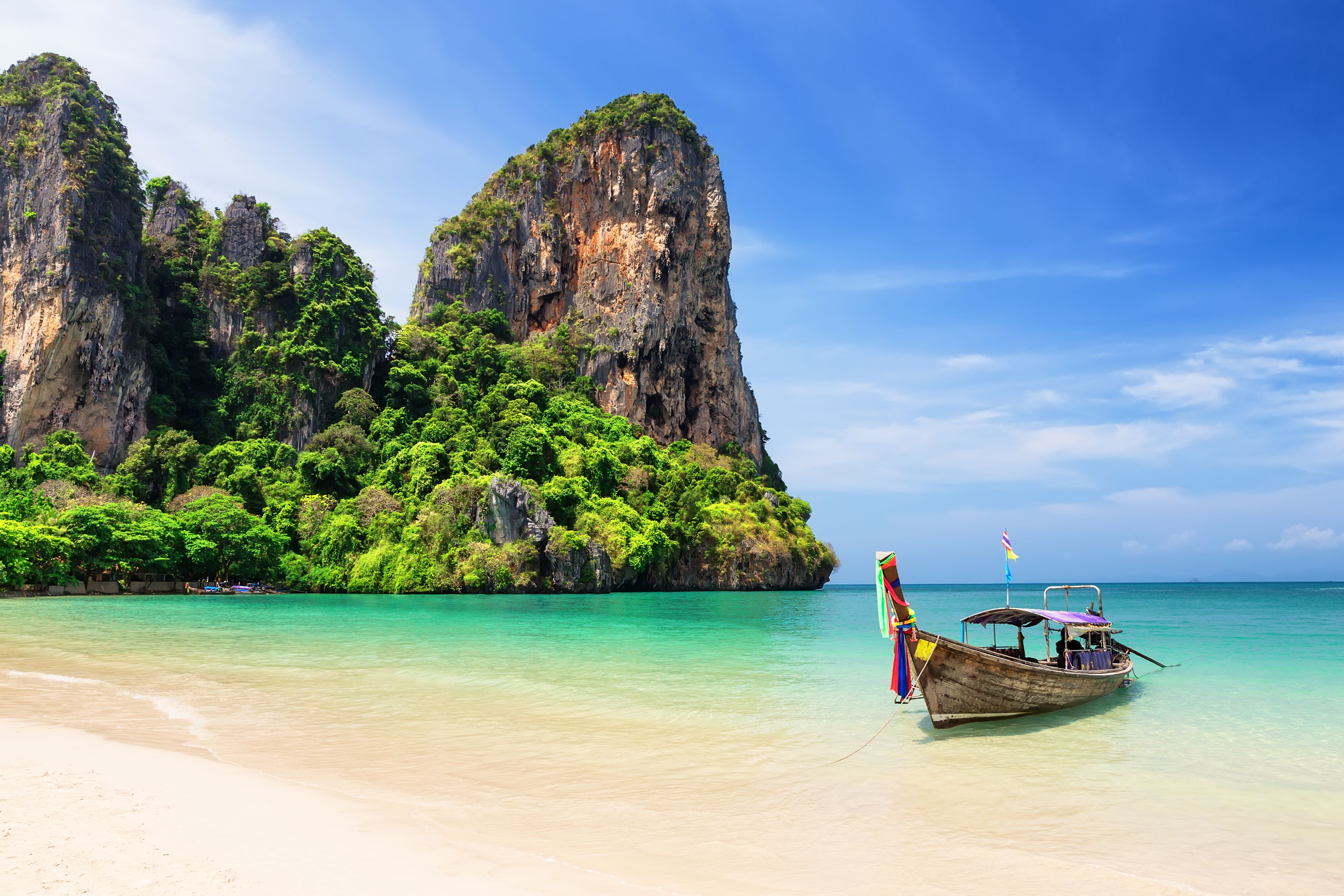 Langheckboot am Strand von Railay Beach, türkisfarbenes Meer und grüne Felsen im Hintergrund.
