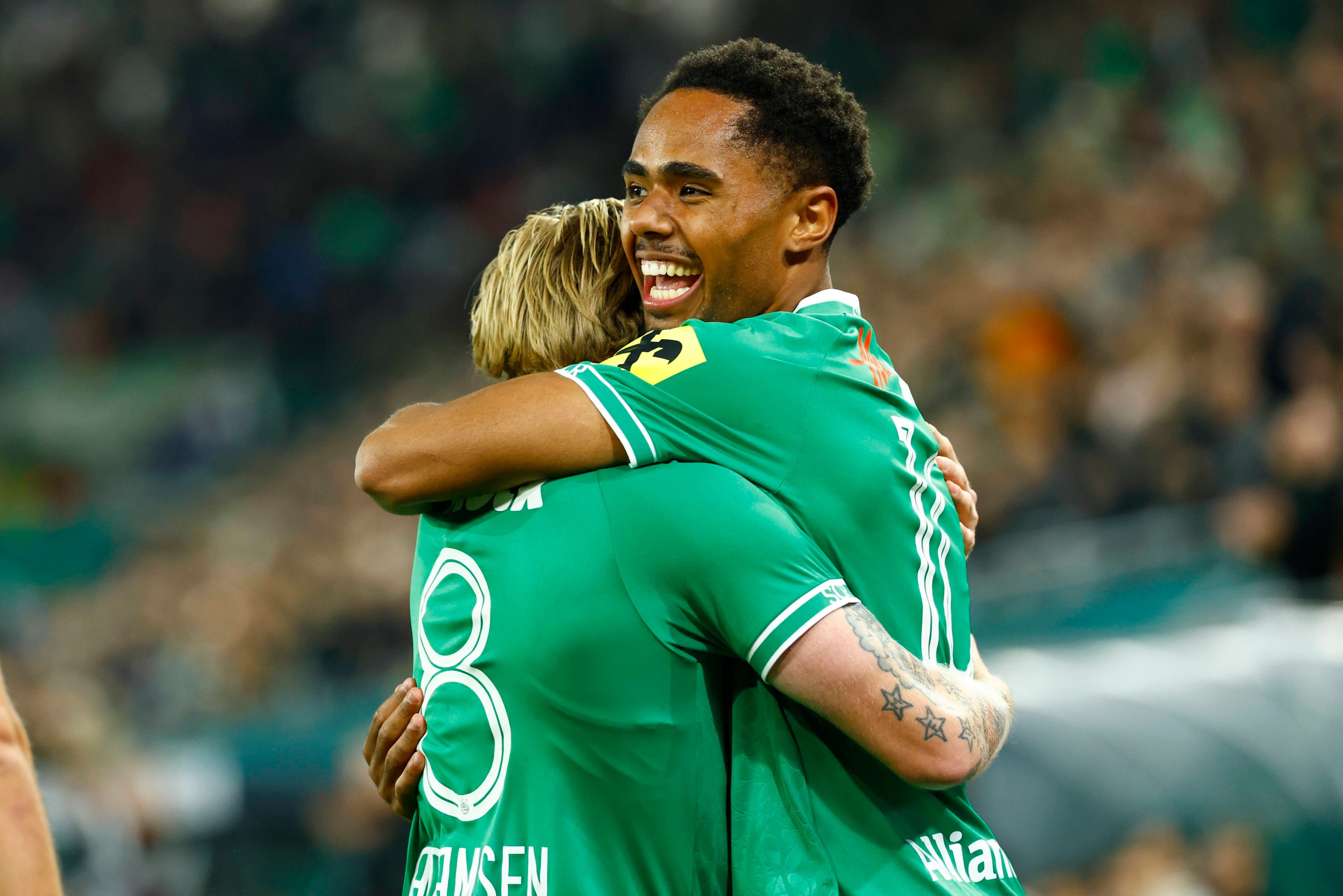 Zwei Rapid Wien-Spieler umarmen sich jubelnd nach einem Tor im Stadion.
