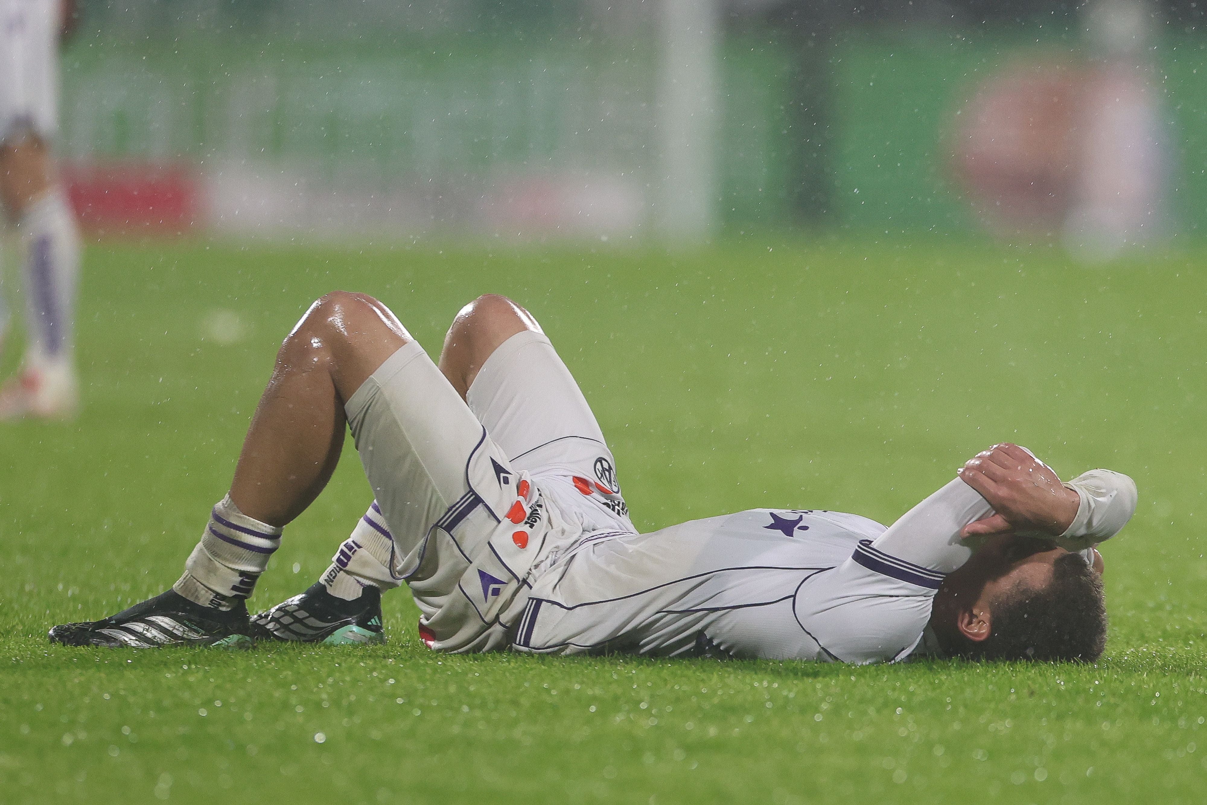 Ein Fußballspieler liegt verletzt und enttäuscht auf dem nassen Rasen.