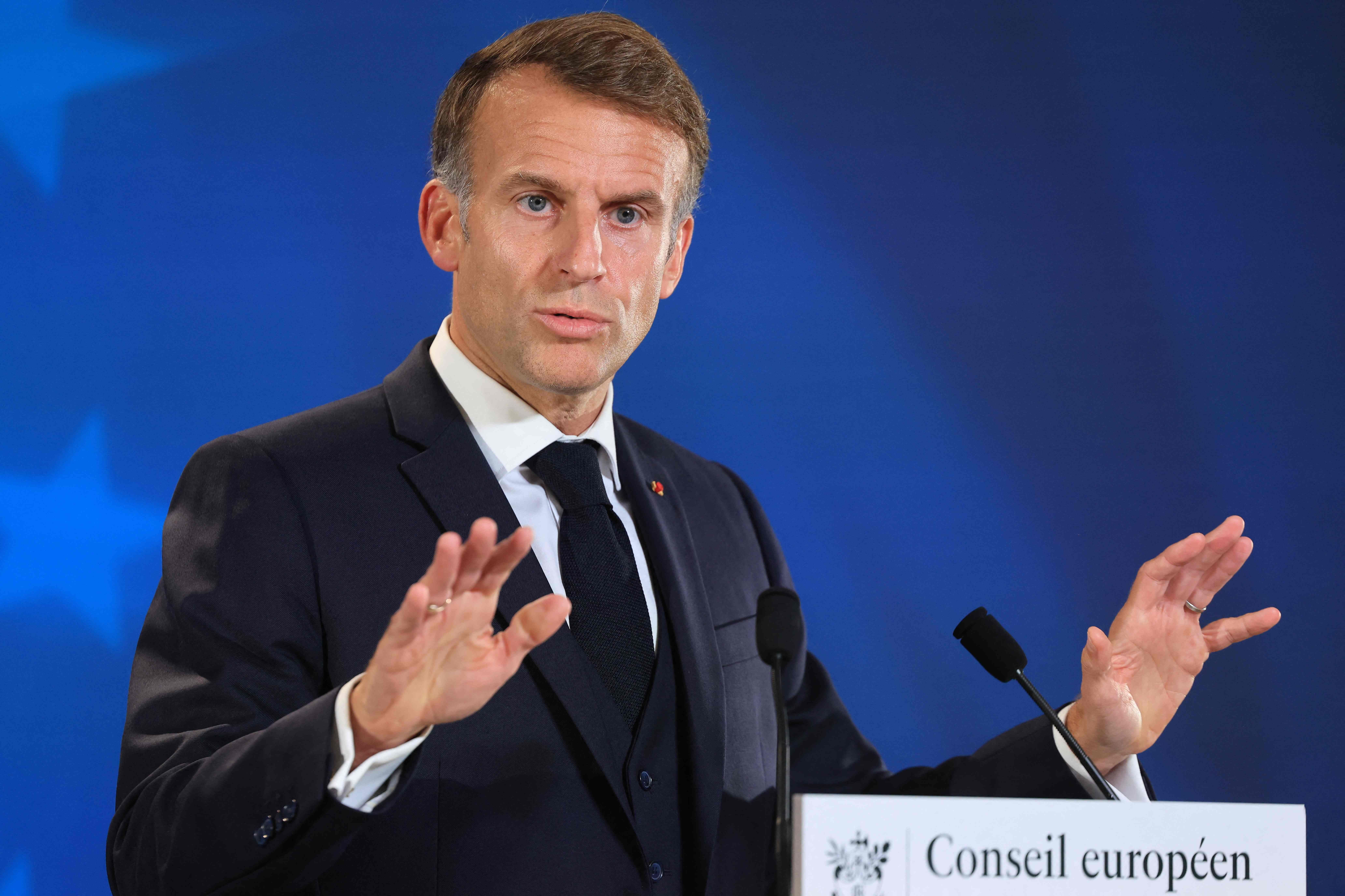 Ein Mann im Anzug spricht auf einer Pressekonferenz vor einem blauen Hintergrund und Mikrofonen.