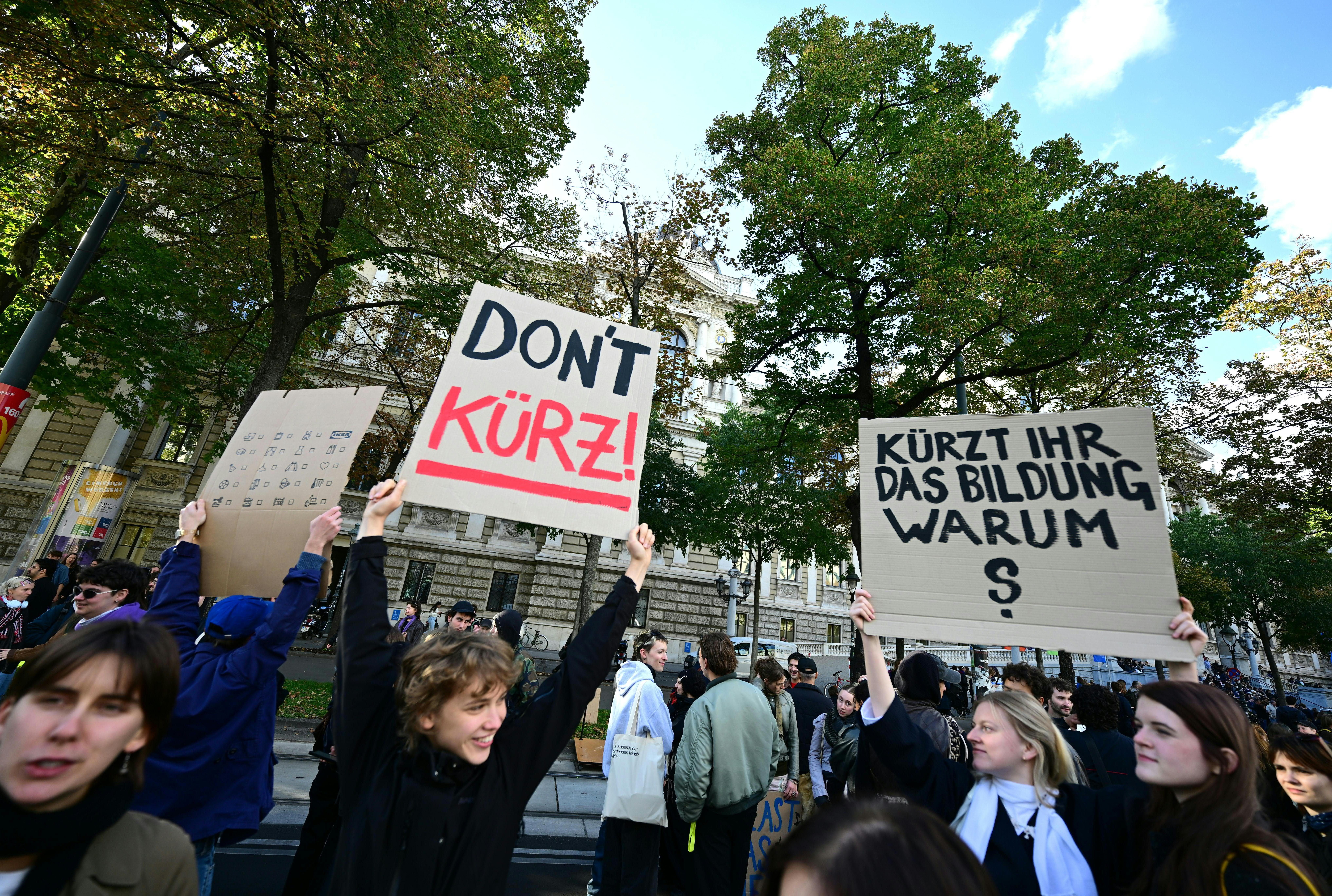 Demonstrierende halten Schilder gegen Bildungskürzungen auf der Ringstraße in Wien hoch.