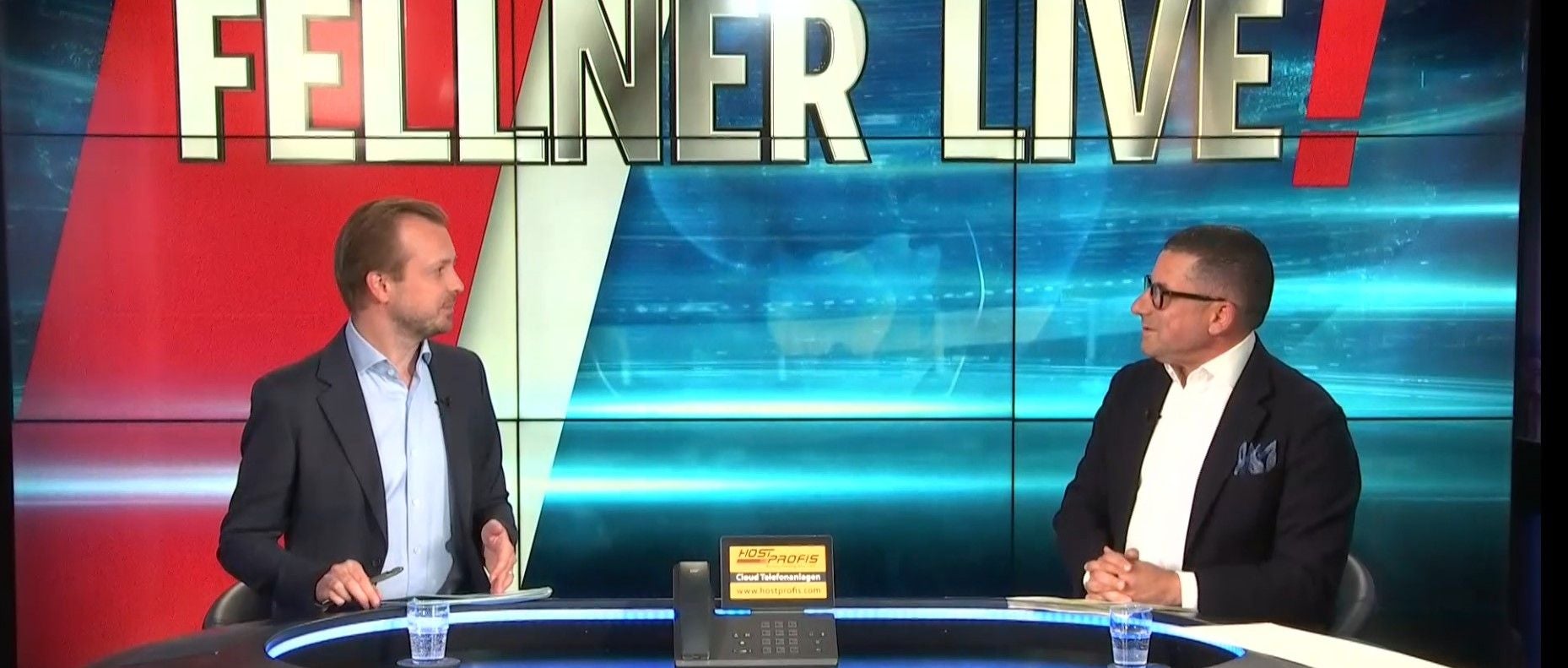 Zwei Männer sitzen im TV-Studio vor „FELLNER LIVE!“-Schriftzug und unterhalten sich.