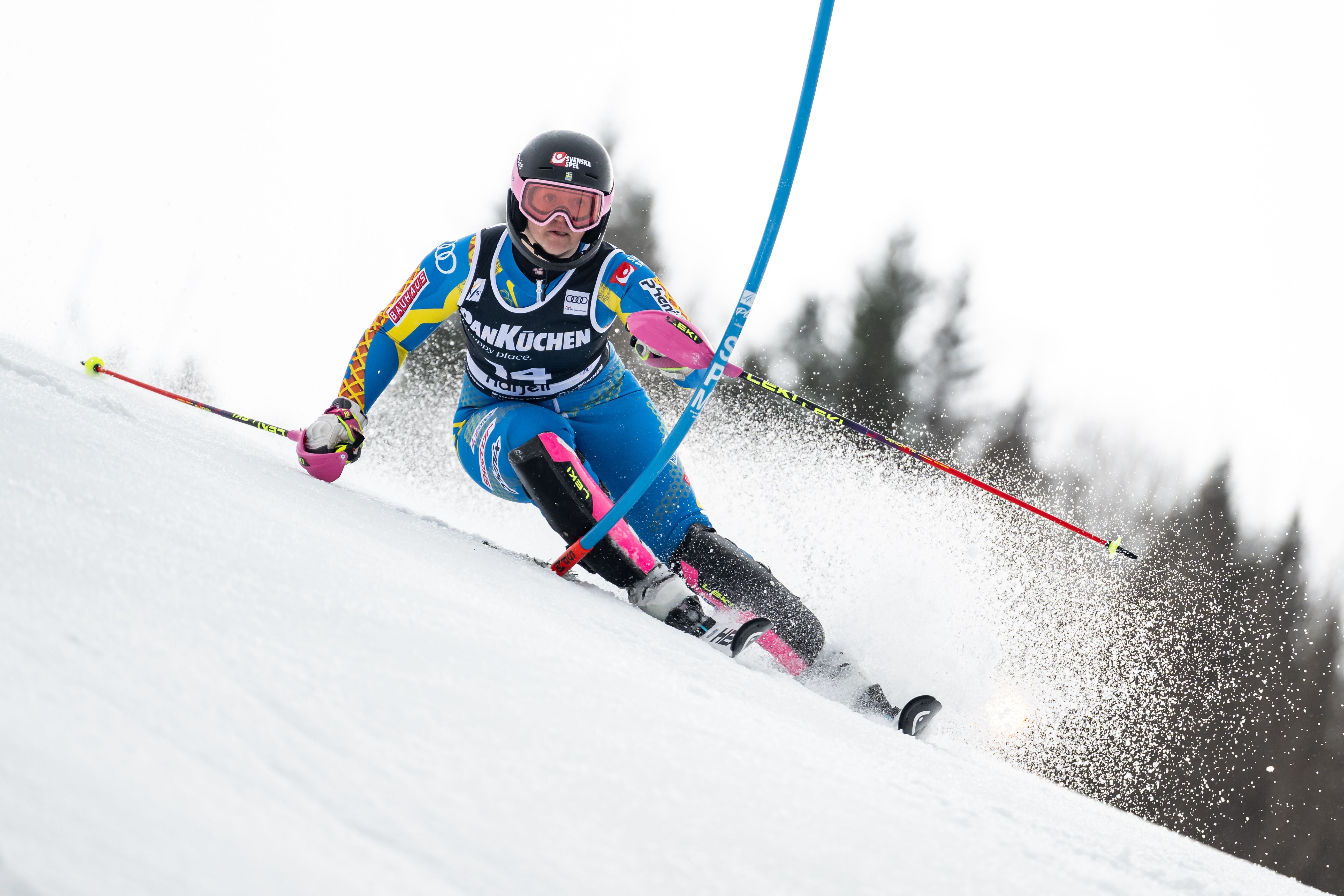 Skirennläuferin fährt durch ein Slalomtor auf einer verschneiten Skipiste.