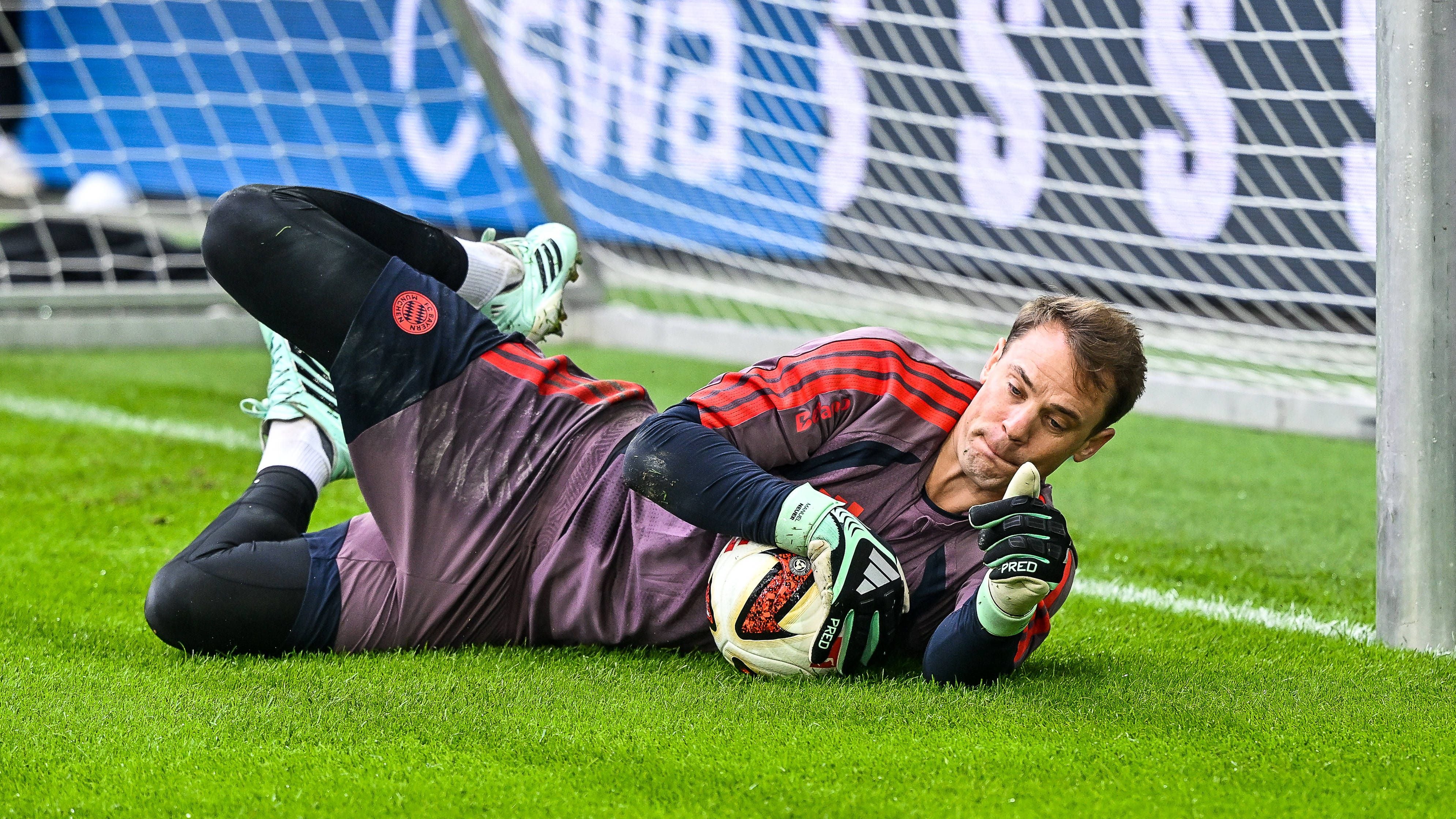 Torwart hält den Ball und zeigt Daumen hoch, liegend vor dem Tor auf dem Fußballfeld.