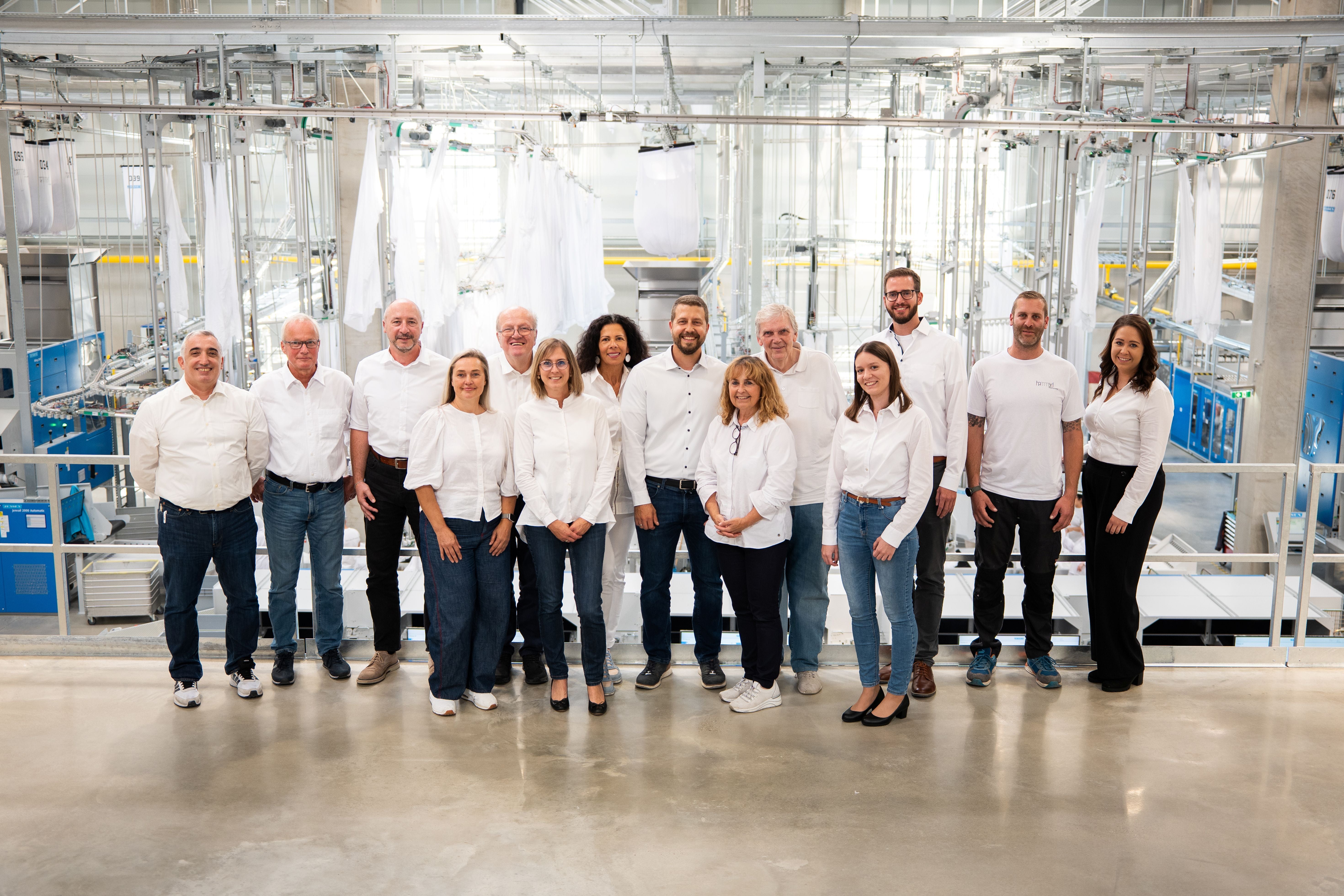 Das Serviceteam der Hammerl Austria Mietwäsche posiert gemeinsam vor Industrieanlagen.